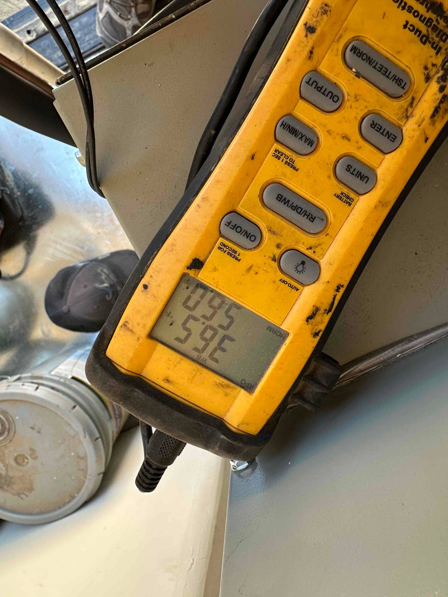 Digital thermometer probe reads 59°F on the display while measuring air temperature at the HVAC installation.