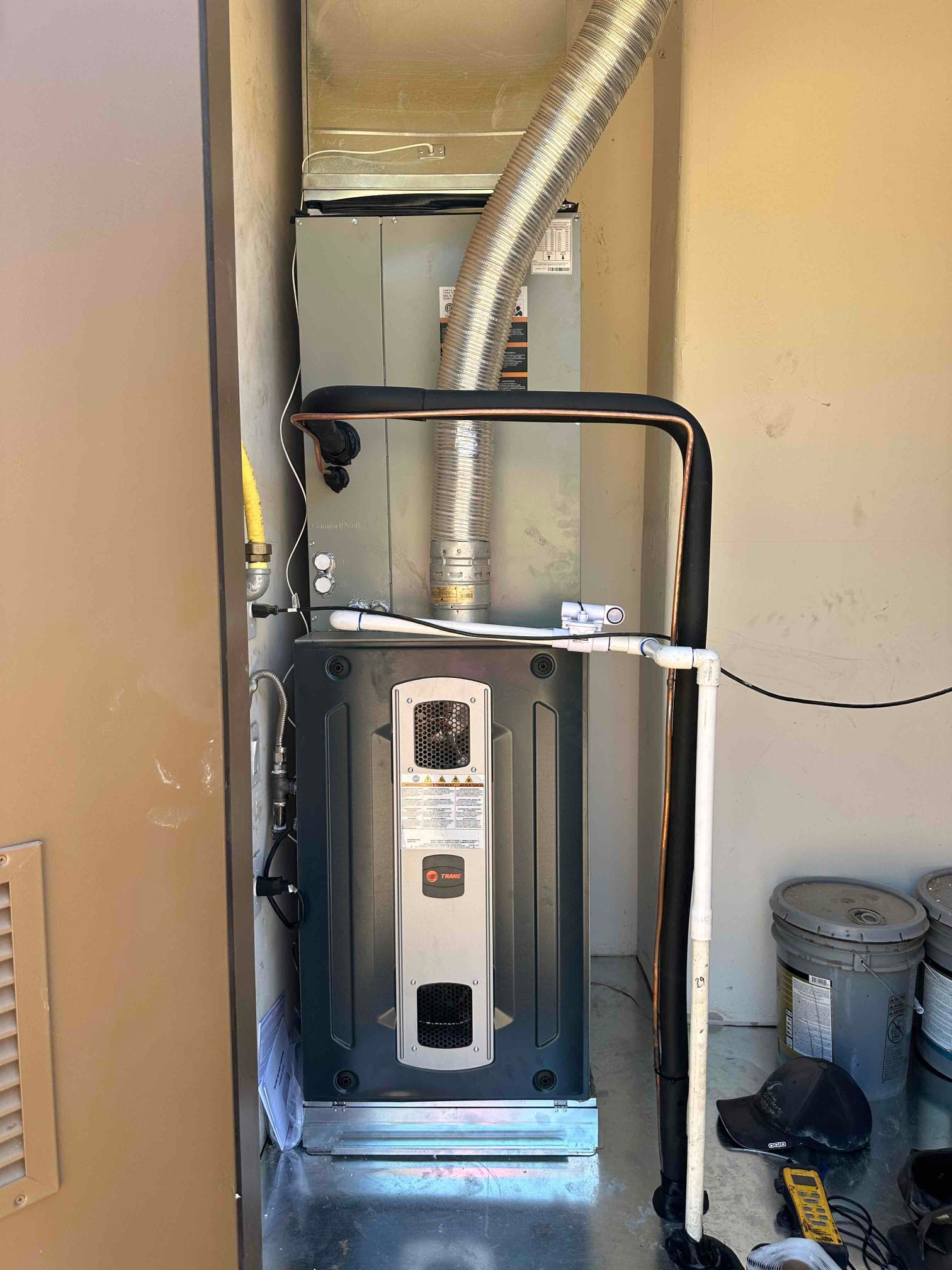 New furnace and evaporator coil installed with venting, condensate drain, insulated refrigerant lines, and gas connection in a utility closet.