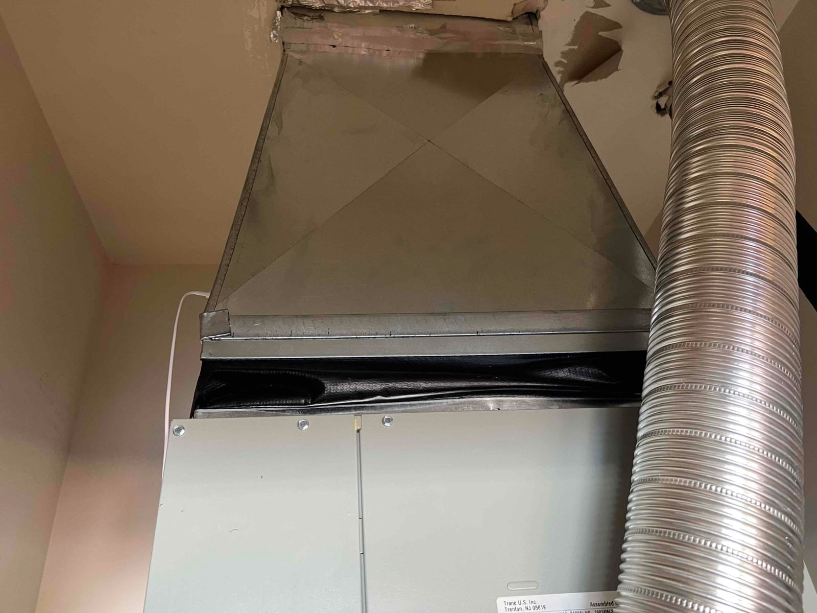 New furnace with sealed sheet metal supply plenum and flexible metal vent duct routed to the side, showing clean installation details.