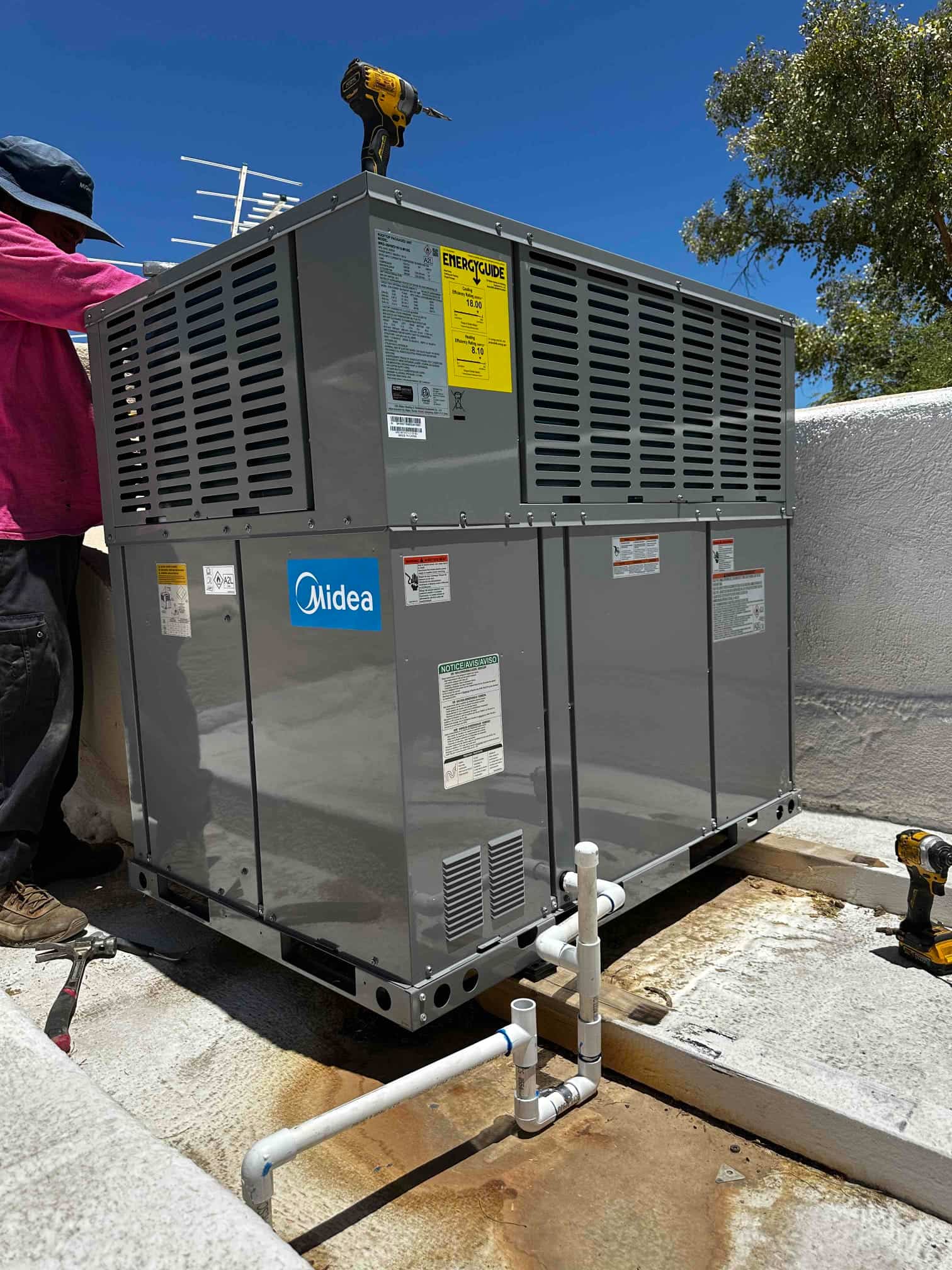 New rooftop packaged HVAC unit set on curb with connected condensate drain piping and tools visible during installation.