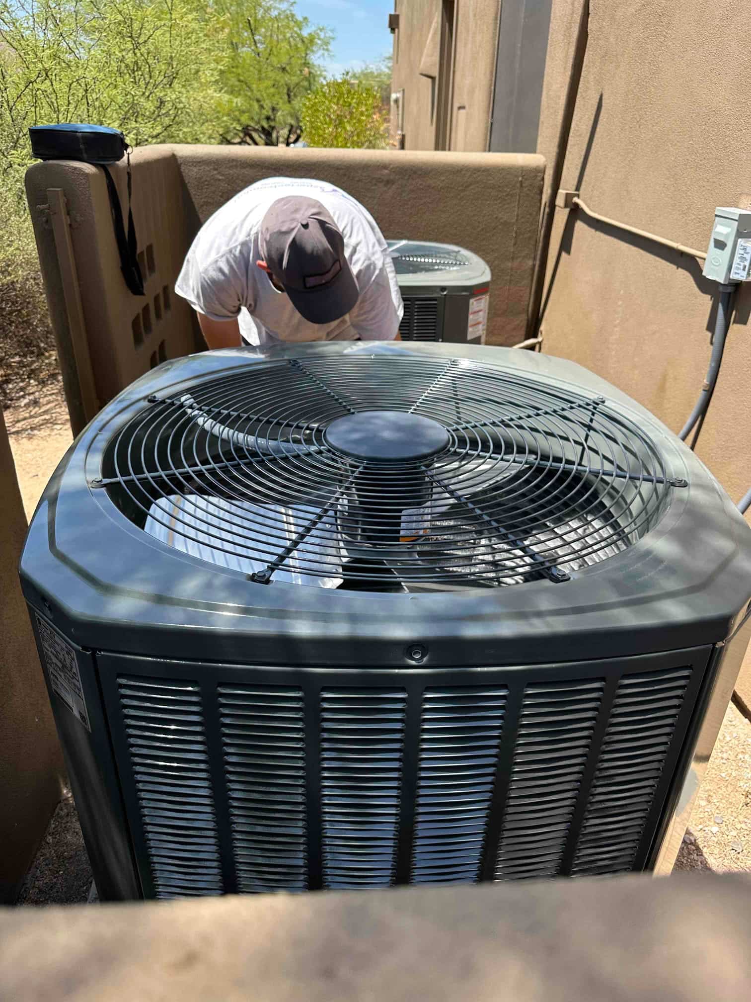 Outdoor condensers installed on pads with protective fan grilles; technician works in the service area beside the units.