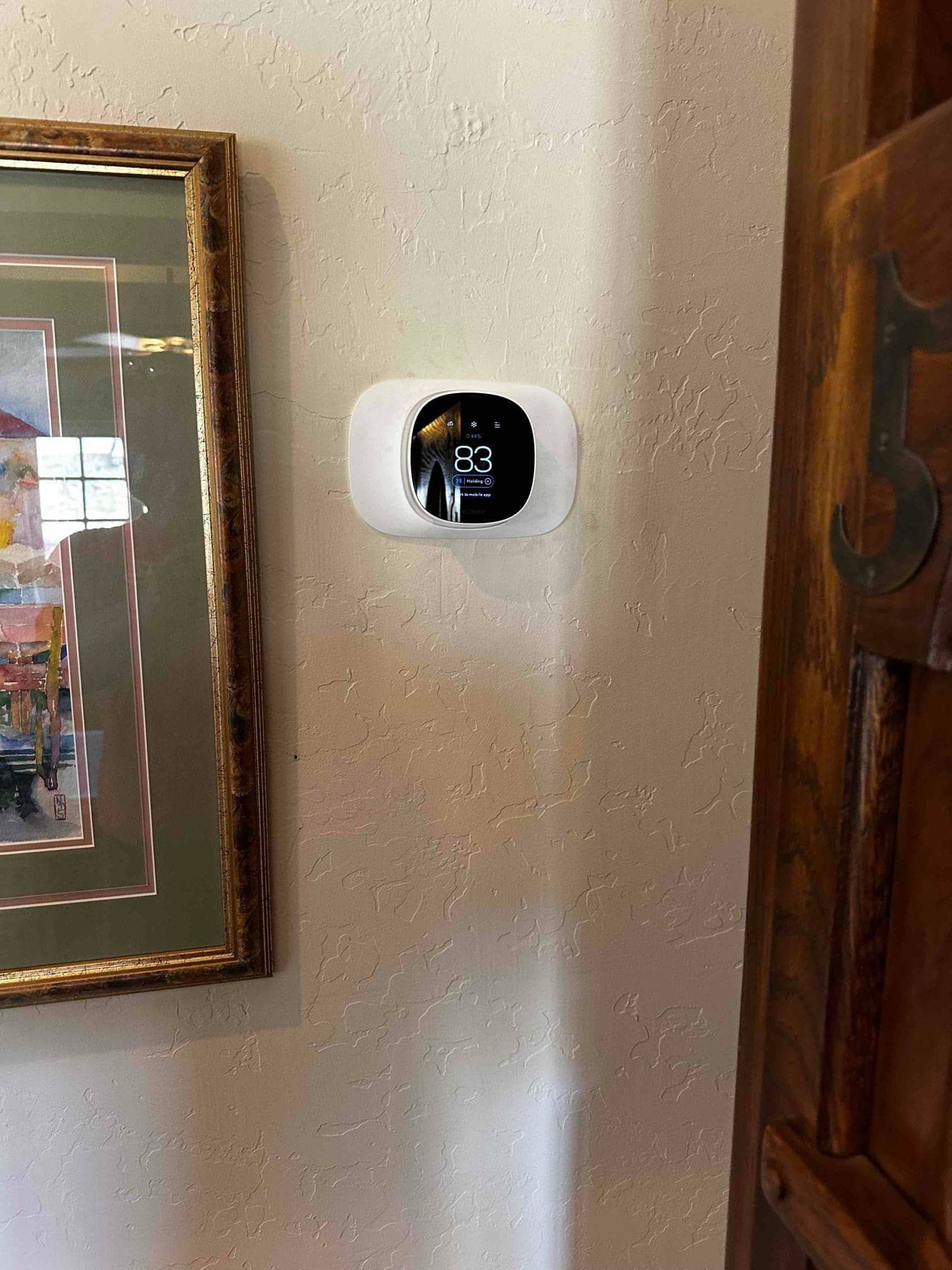 Wall-mounted smart thermostat installed and powered, displaying indoor temperature and system status on its screen.
