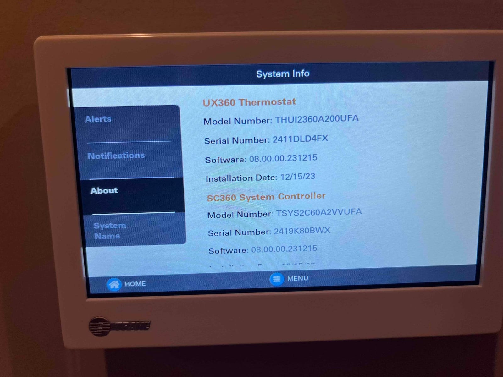Wall-mounted touchscreen thermostat displays system information on the About screen after installation.