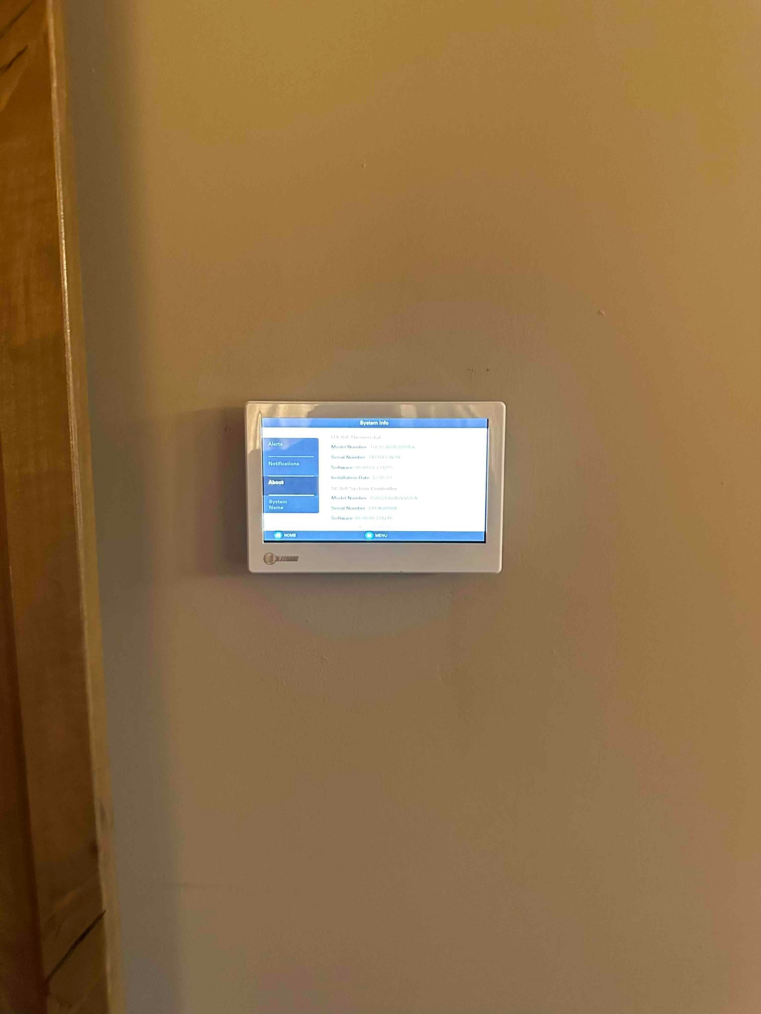 Wall-mounted touchscreen thermostat installed and powered on, displaying system information menu after commissioning.