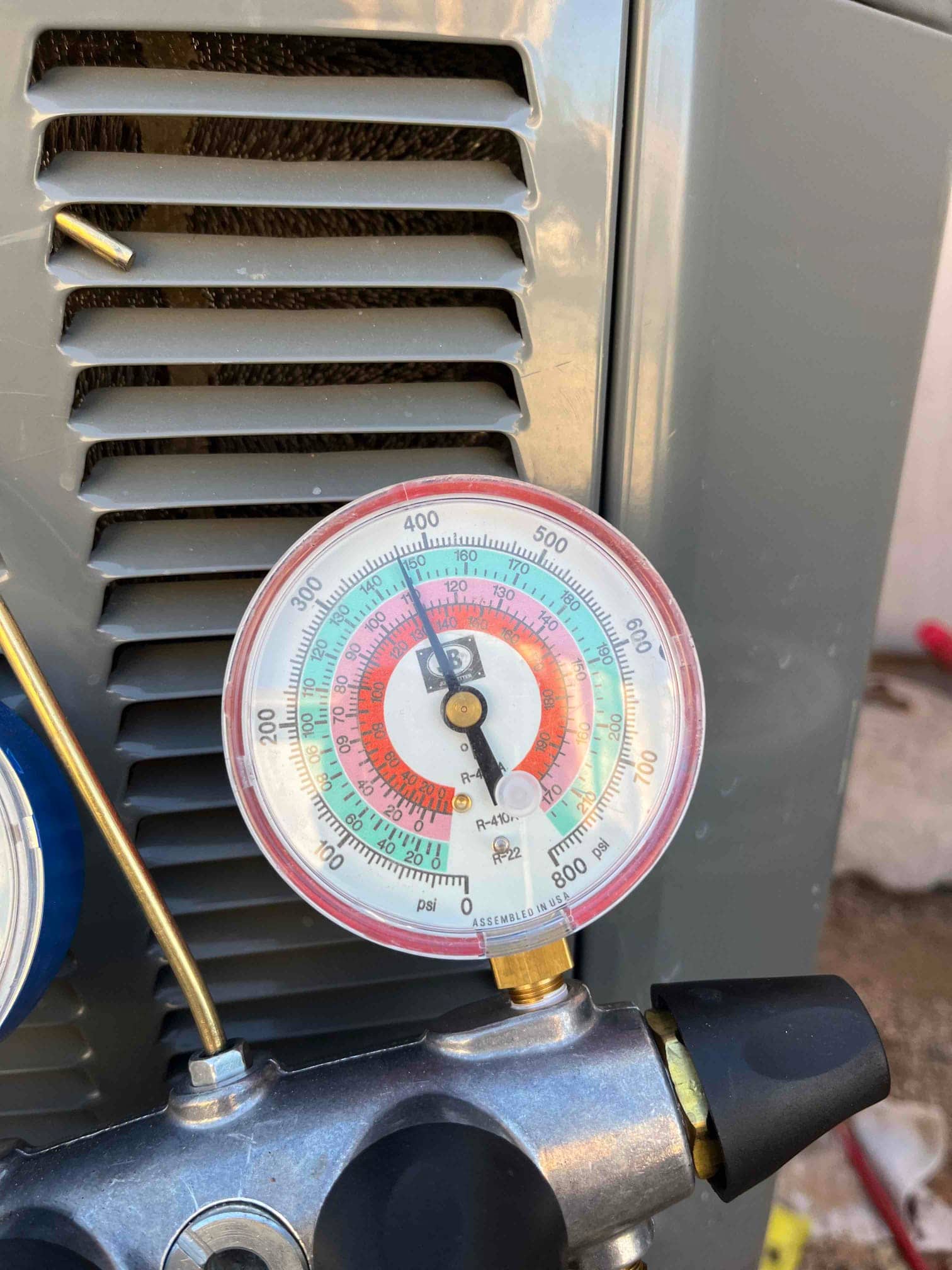 Analog manifold gauge connected at the outdoor unit shows low-side pressure at 118 psi during system operation.