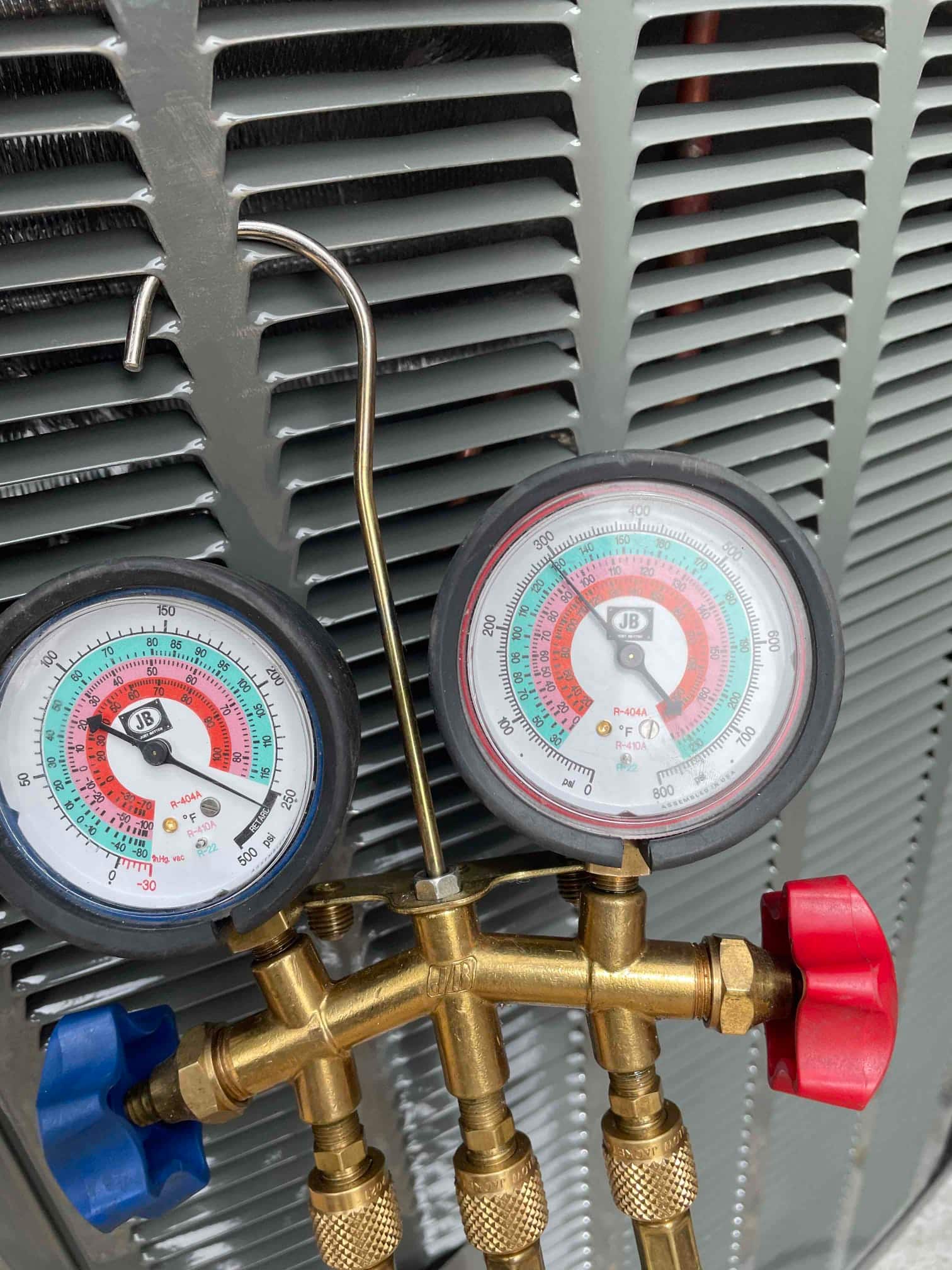 Analog manifold gauge set hangs on the outdoor condenser during HVAC installation, ready for system testing and charging.