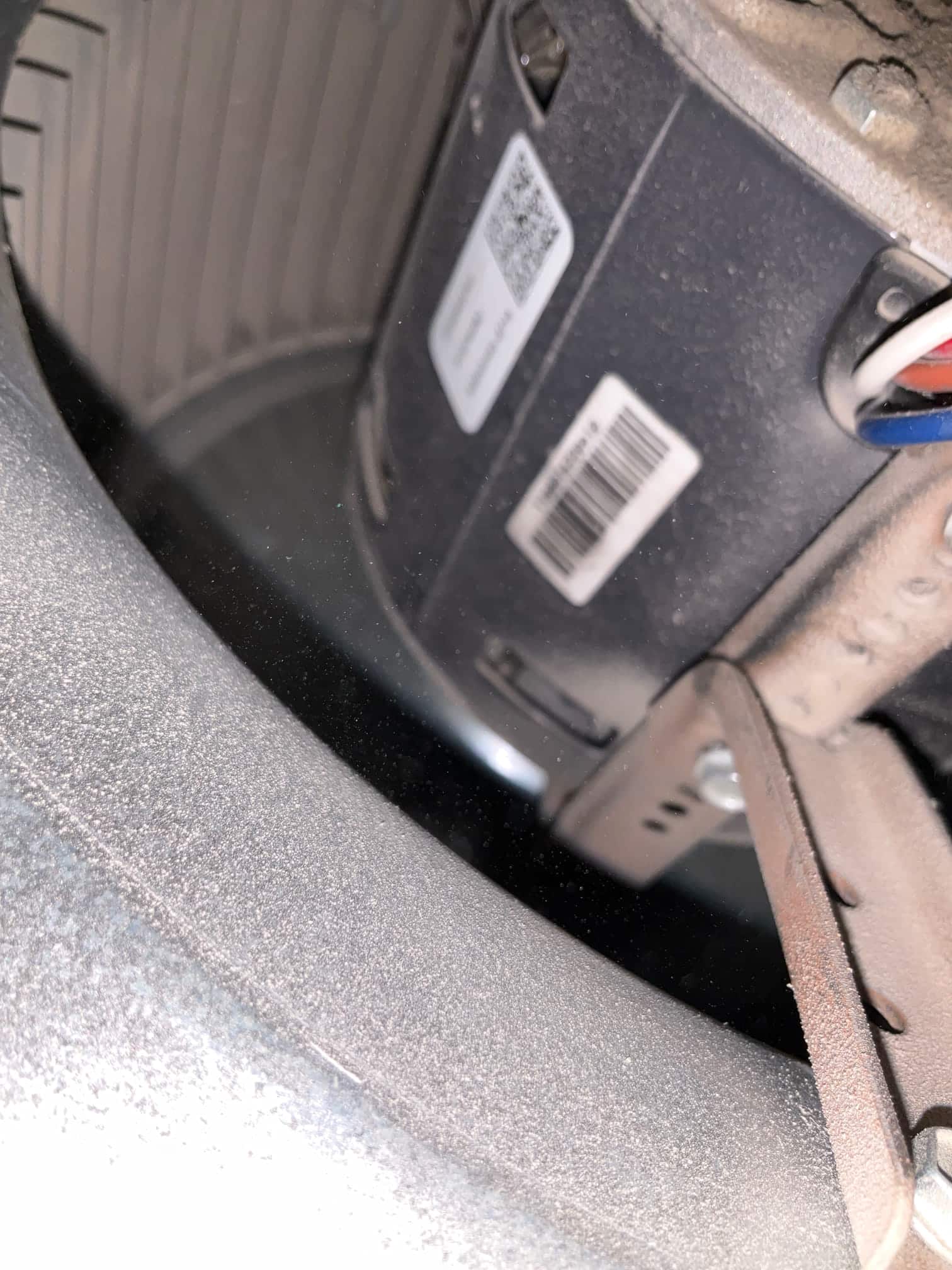 Blower wheel and motor inside the air handler, showing dusty housing, barcode labels, mounting bracket, and connected wiring.
