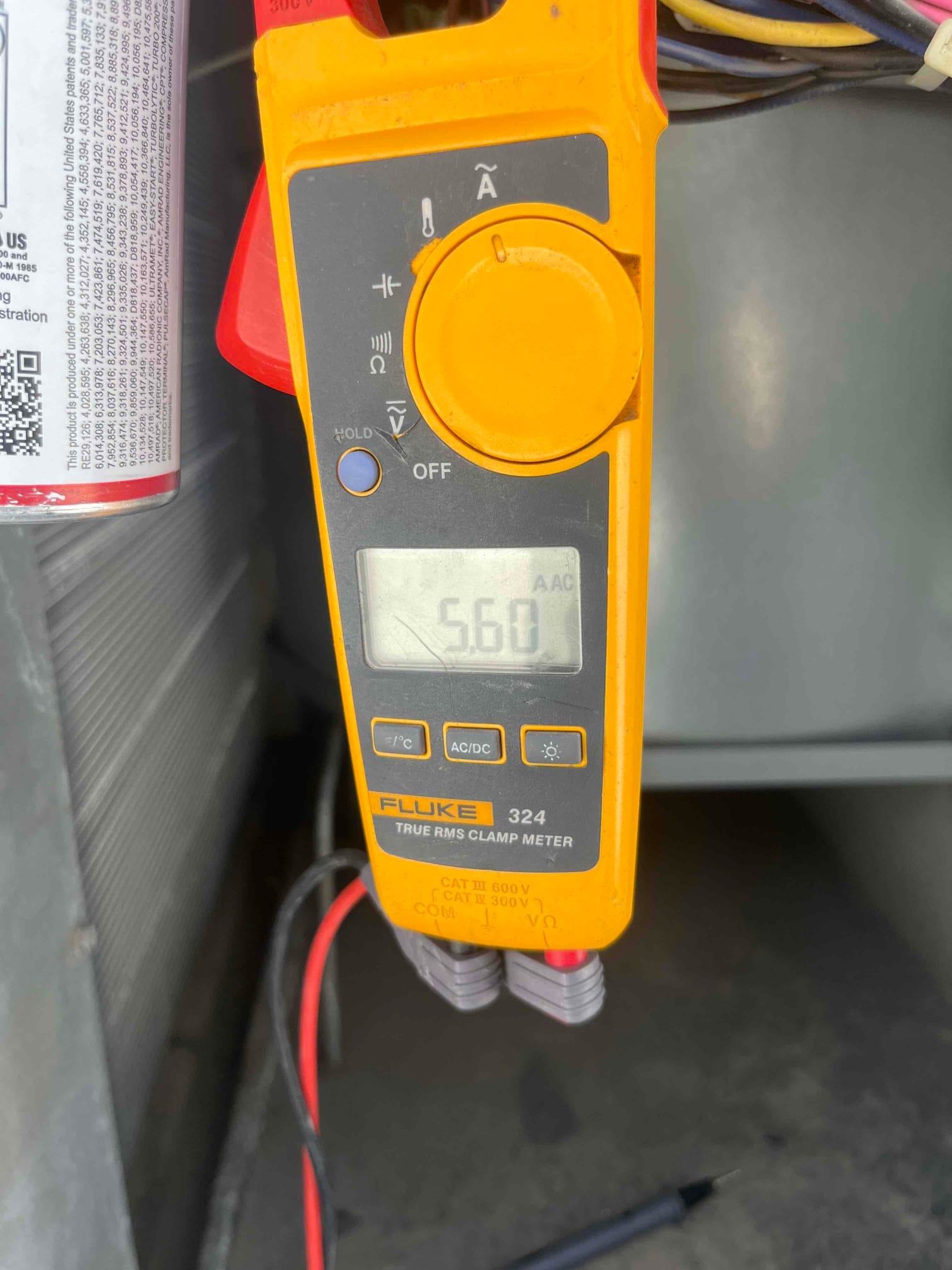 Clamp meter displays 5.60 A AC while measuring current on a conductor inside the outdoor condenser compartment.