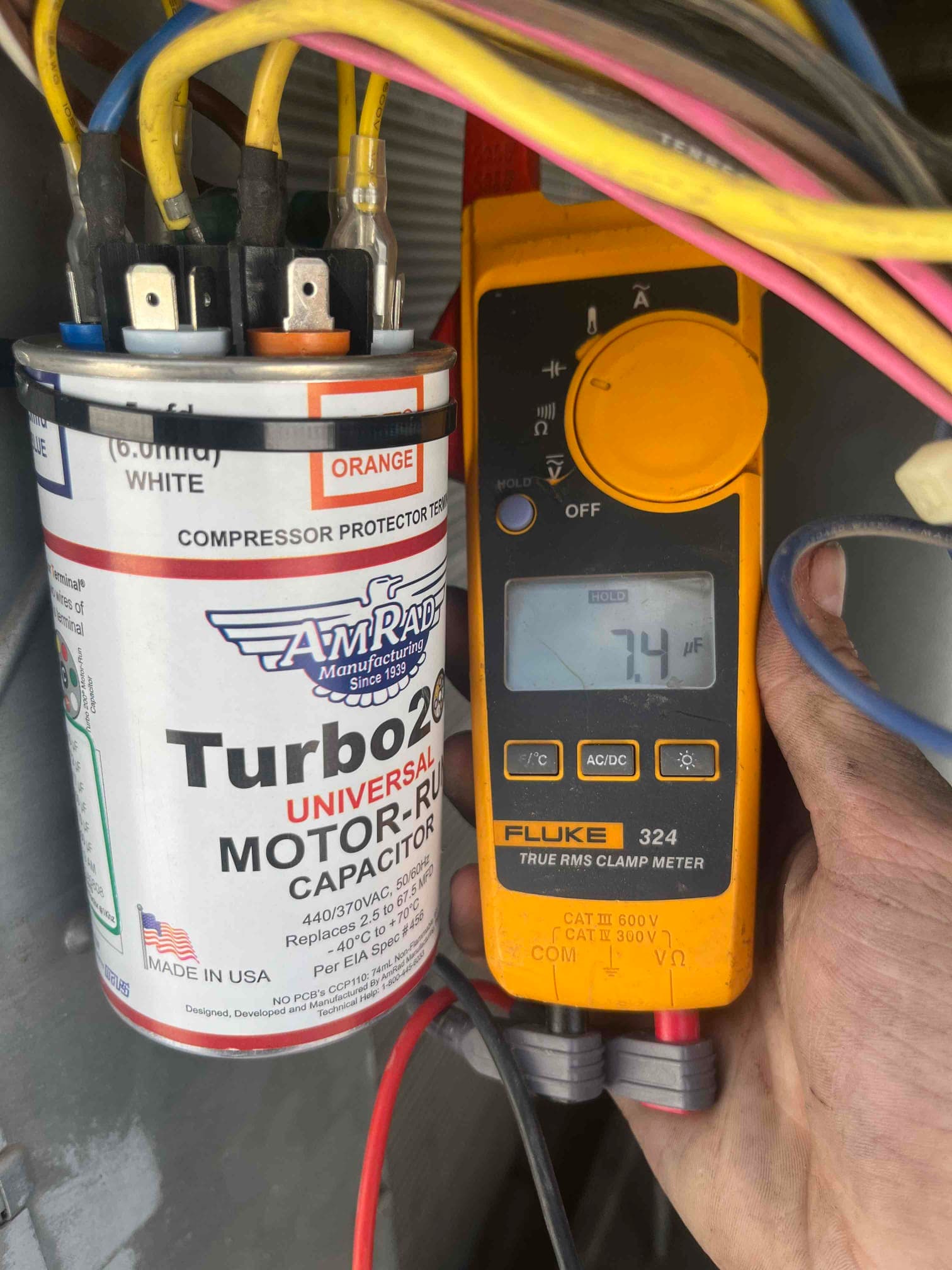 Clamp meter shows 7.4 A on the condenser fan motor lead next to the installed dual-run capacitor.