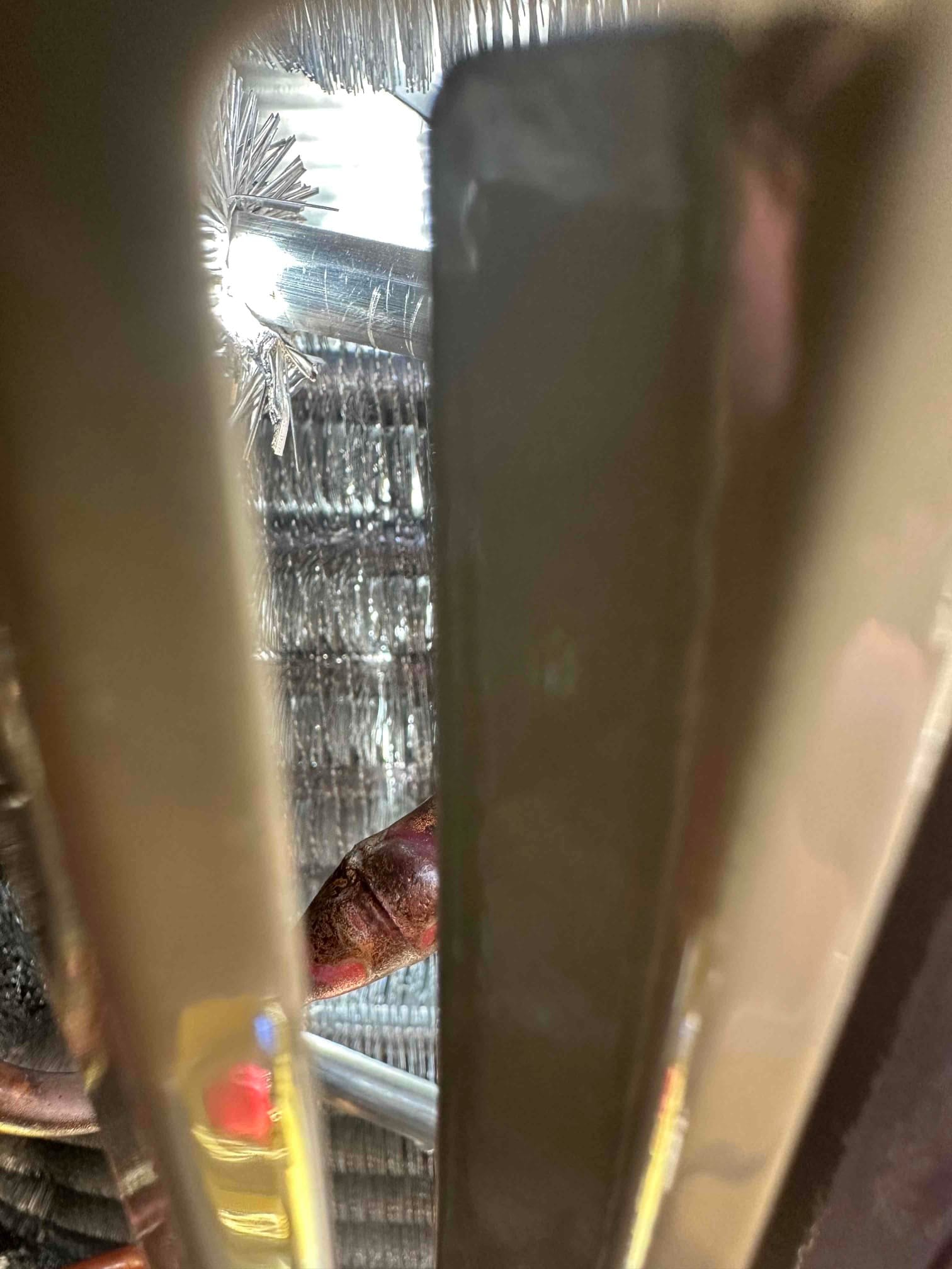 Close-up view through the condenser grille showing coil fins, a refrigerant tube, and internal tubing connections.