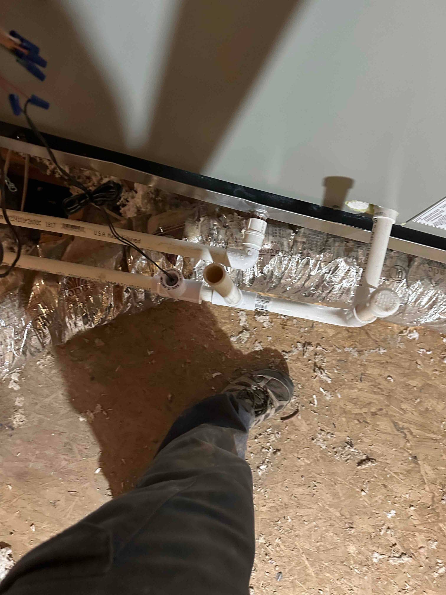 Condensate drain piping with cleanout and trap installed beneath the indoor unit, routed across the attic floor with insulation visible.