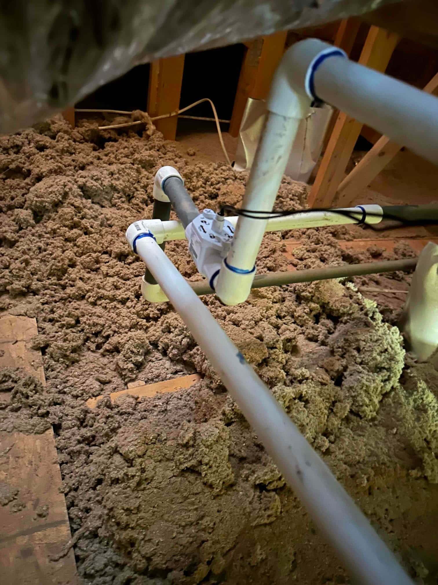 Condensate drain piping with PVC fittings installed in attic insulation near the air handler location.