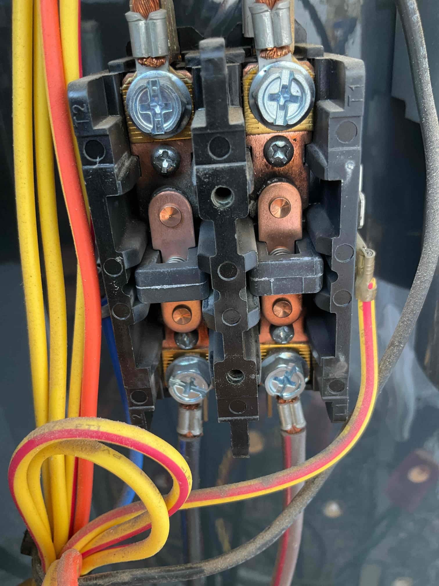 Contactor assembly inside outdoor condenser, with multiple yellow, red, and blue wires secured to screw terminals.