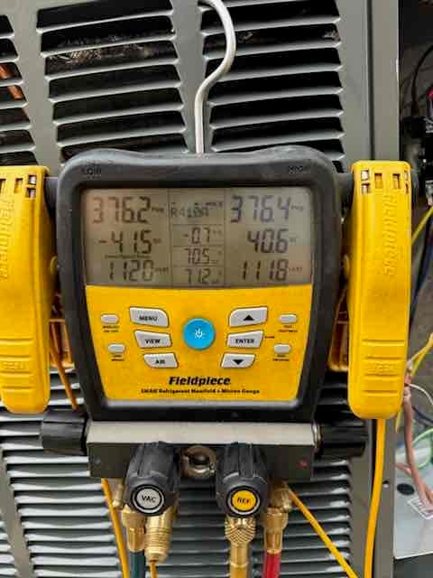 Digital manifold connected to the condenser shows operating suction and liquid pressures with temperature clamps attached during system commissioning.