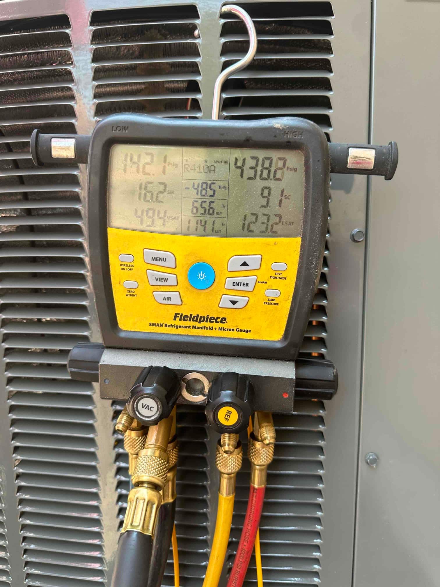 Digital manifold connected at the outdoor unit shows operating pressures of 142 PSI suction and 438 PSI liquid with R-410A selected.