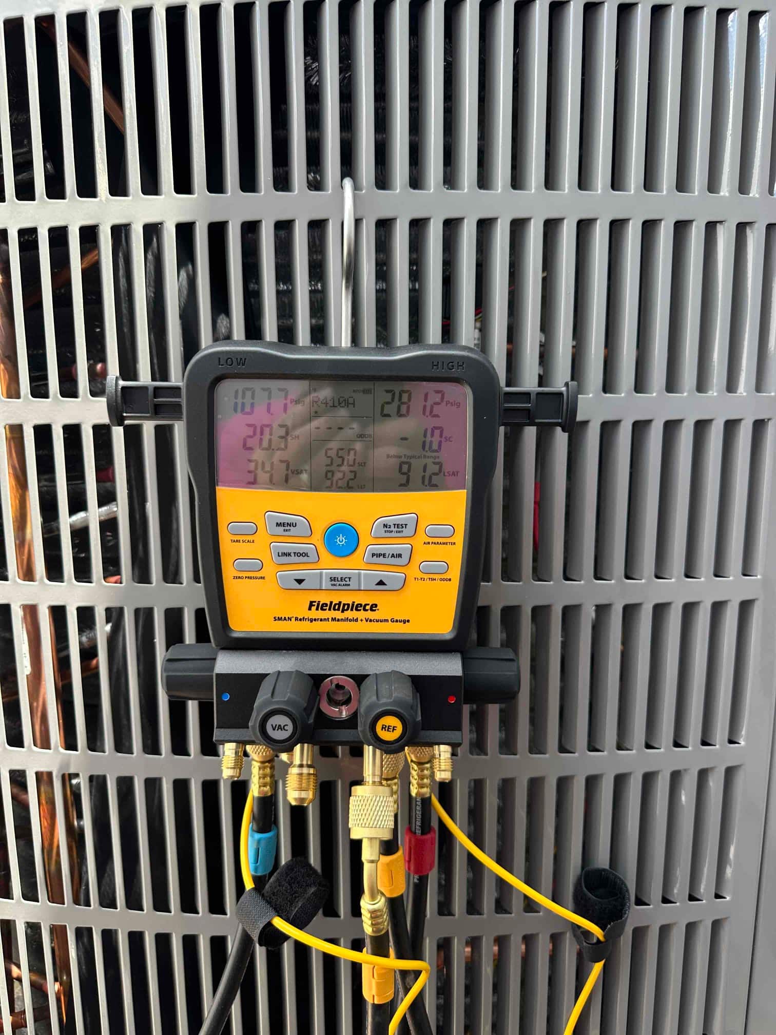 Digital manifold connected to the outdoor unit shows operating pressures and temperatures while the heat pump runs during commissioning.