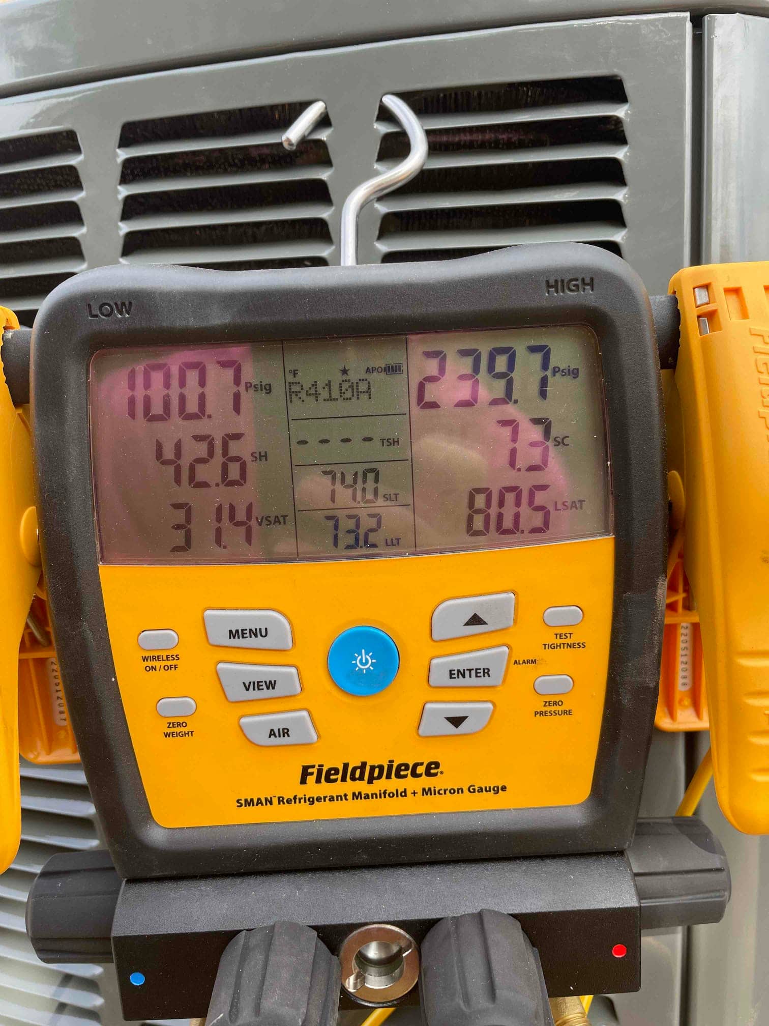 Digital manifold on the outdoor unit shows operating pressures during commissioning, with refrigerant type labeled and superheat and subcooling displayed.