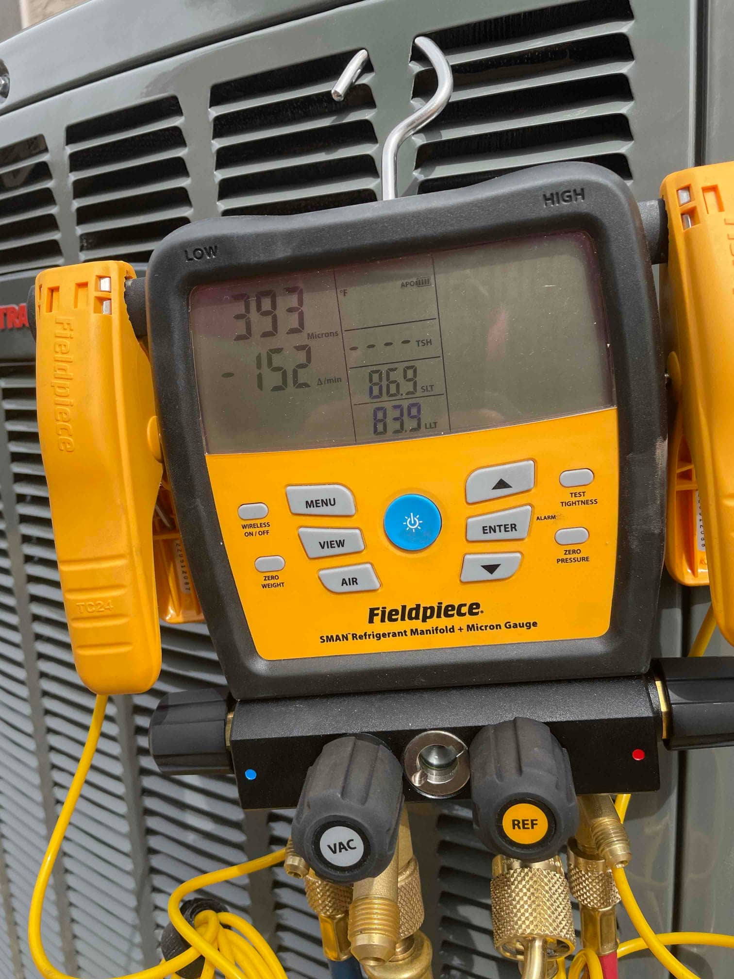 Digital manifold on the outdoor unit shows operating pressures with low and high sides connected during system commissioning.