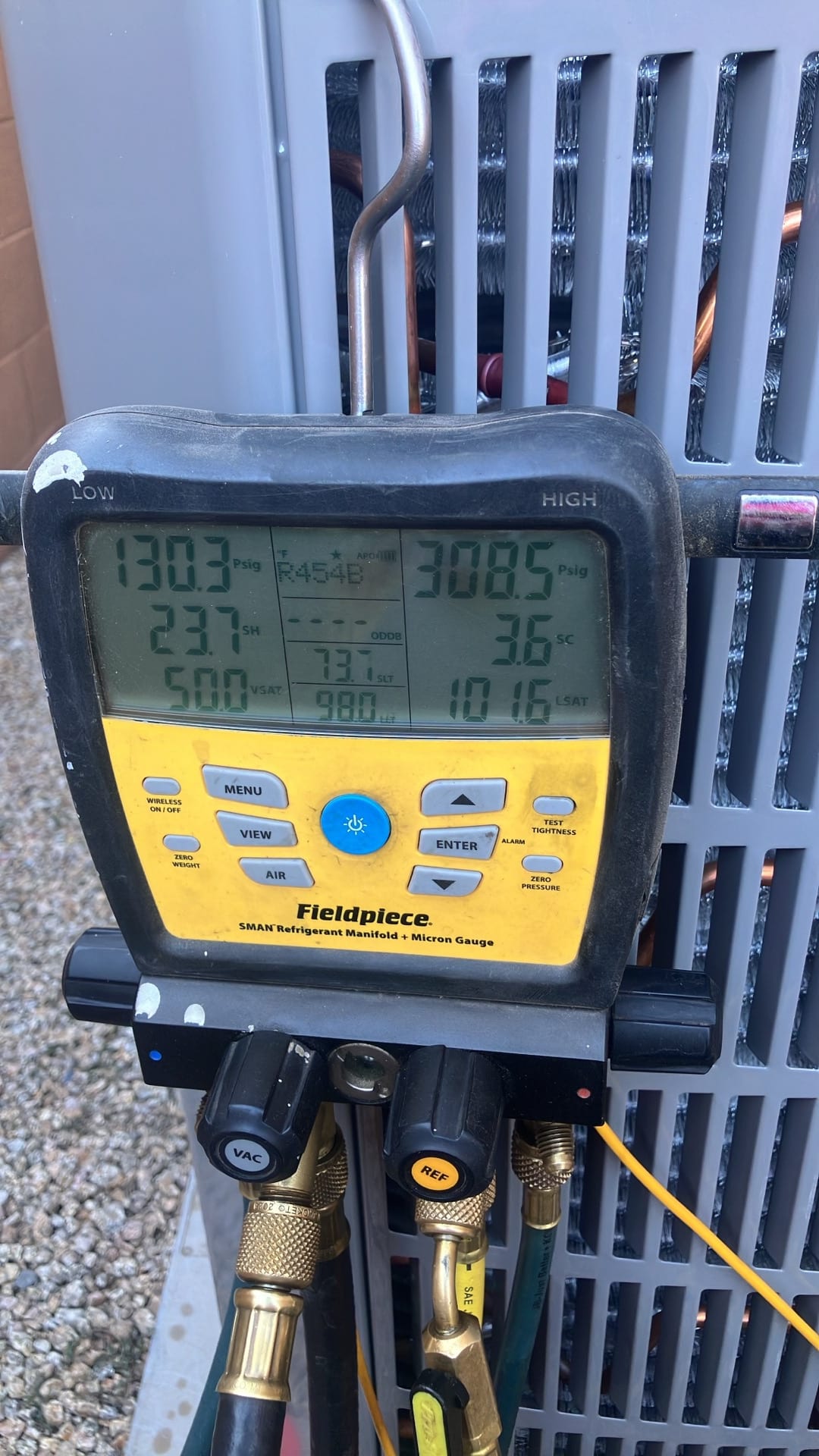 Digital manifold shows system operating pressures with R-454B selected during startup checks at the outdoor condenser.