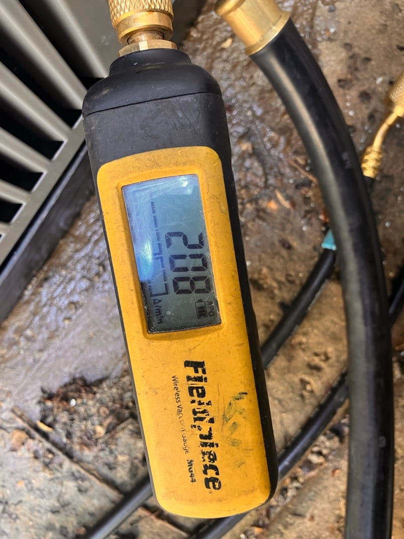 Digital micron gauge connected at the condenser shows 208 microns during system evacuation prior to refrigerant charging.