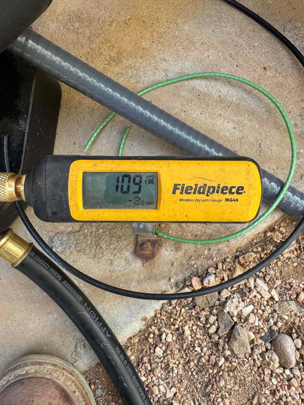Digital micron gauge connected during evacuation shows 109 microns, confirming a deep vacuum before charging the new system.
