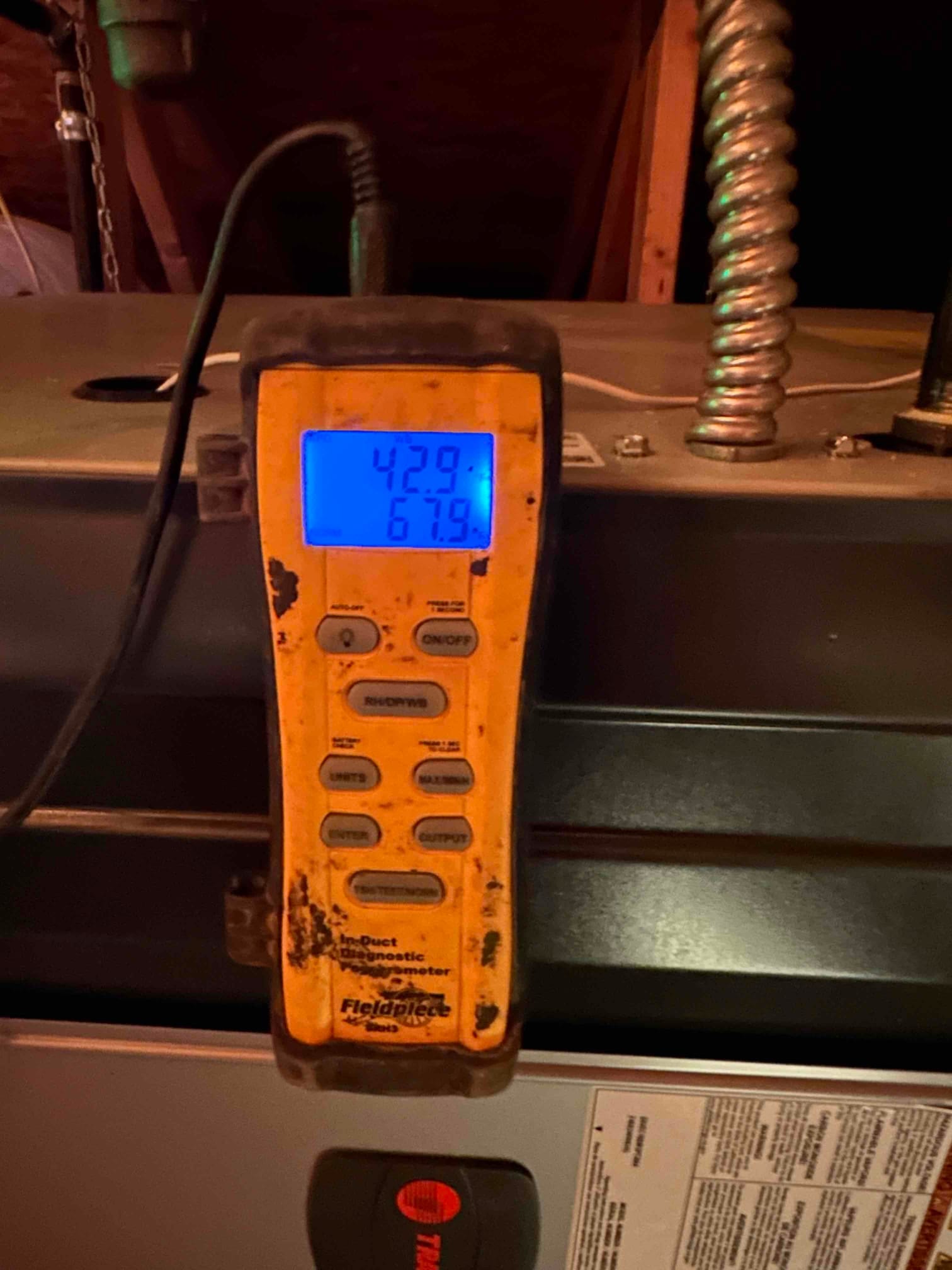 Digital thermometer on the air handler displays 42.9 and 67.9 degrees during airflow temperature checks.