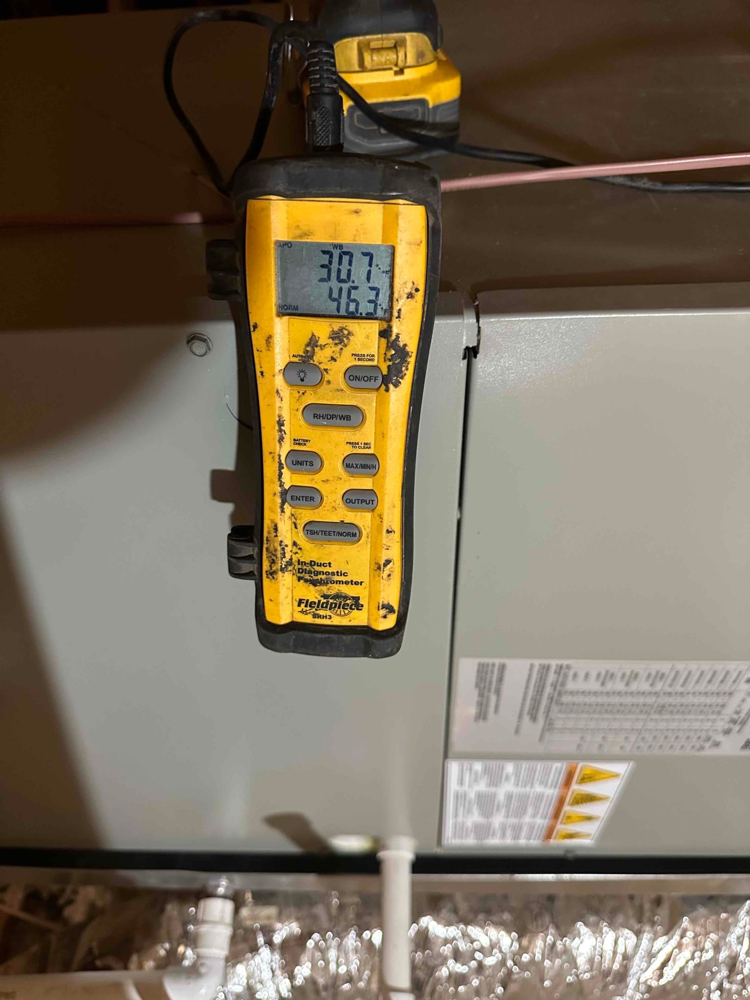 Digital thermometer attached near the air handler displays two temperature readings during airflow measurement for system commissioning.