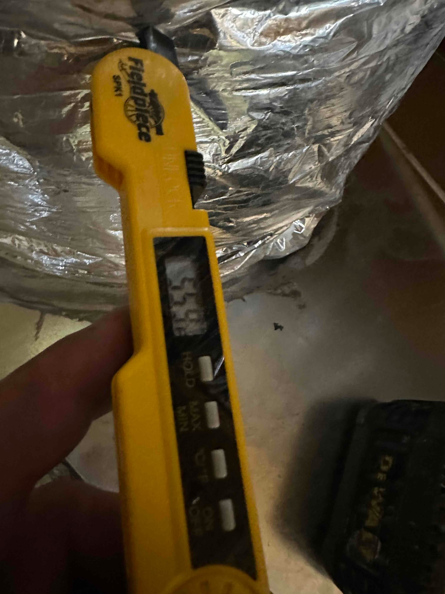 Digital thermometer probe inserted into insulated duct measuring air temperature; display shows 57.4 degrees Fahrenheit.