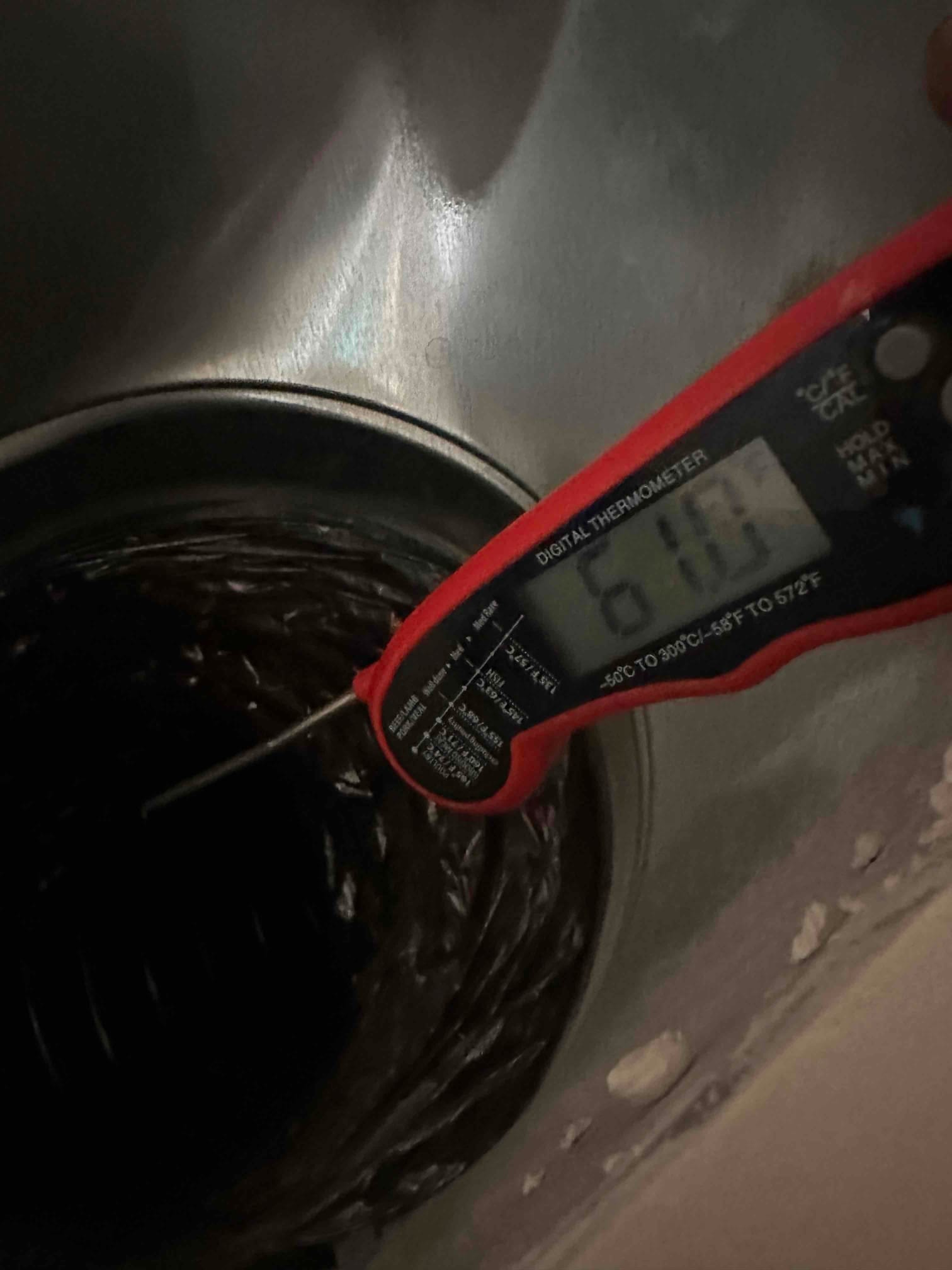 Digital thermometer probe inserted into a round duct opening reads 61°F, documenting supply air temperature during cooling.