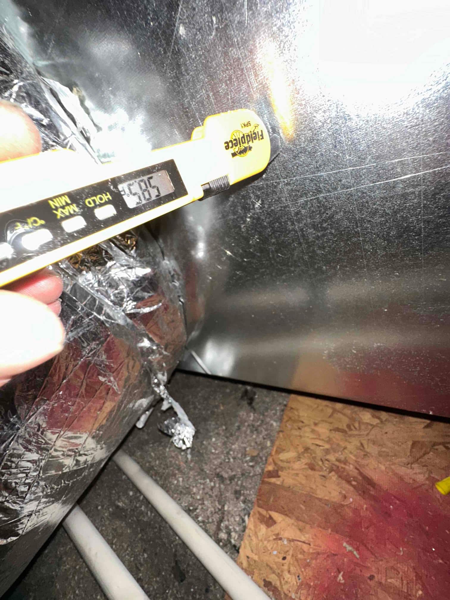 Digital thermometer probe measures air temperature at the duct surface during commissioning, displaying 58.5 degrees Fahrenheit.