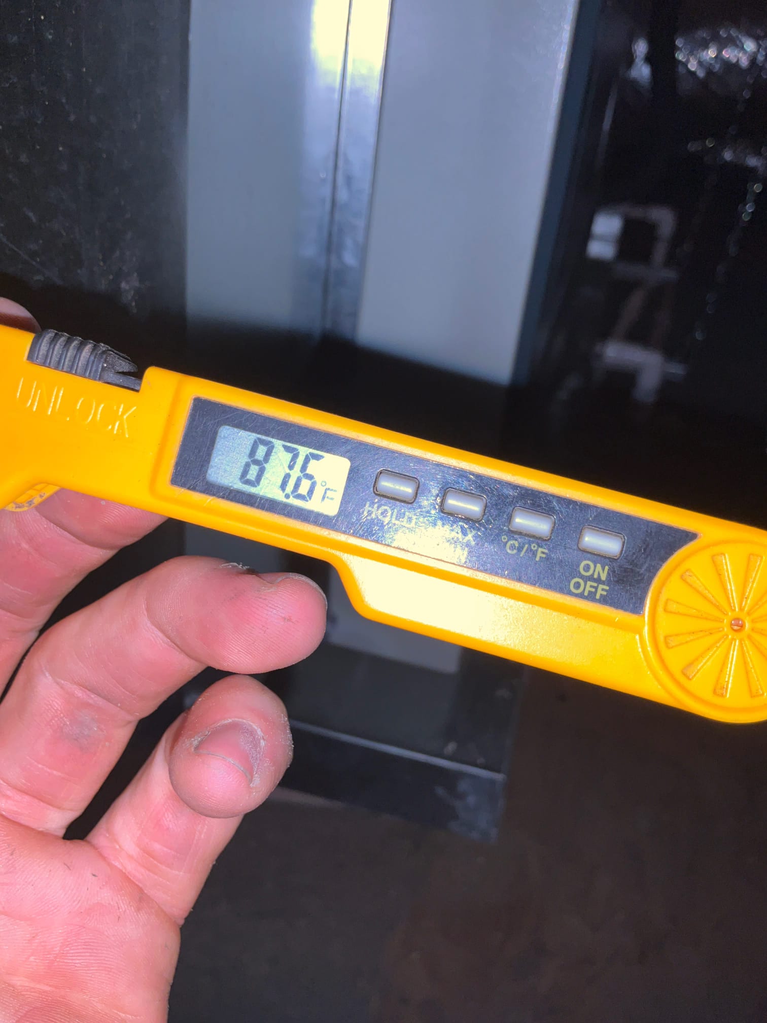 Digital thermometer shows 87.6°F while checking air temperature near the ductwork during commissioning.