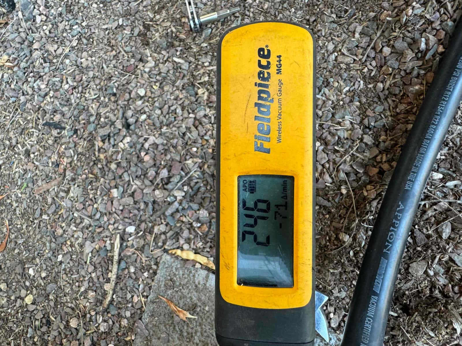 Digital vacuum gauge shows 246 microns during system evacuation beside a vacuum-rated hose at the outdoor unit.