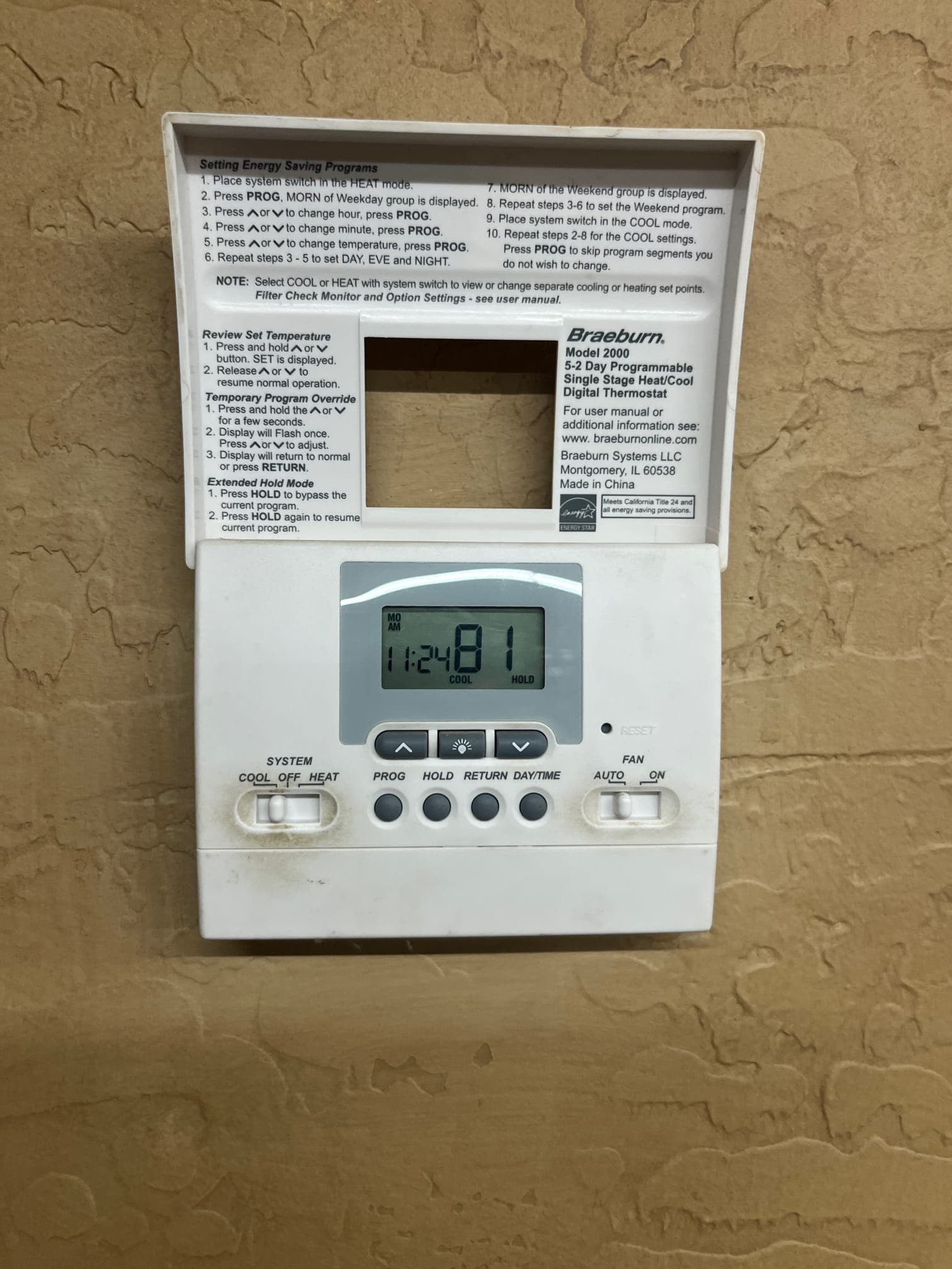 Digital wall thermostat with cover open shows 81°F room temperature and system set to COOL with fan on AUTO.