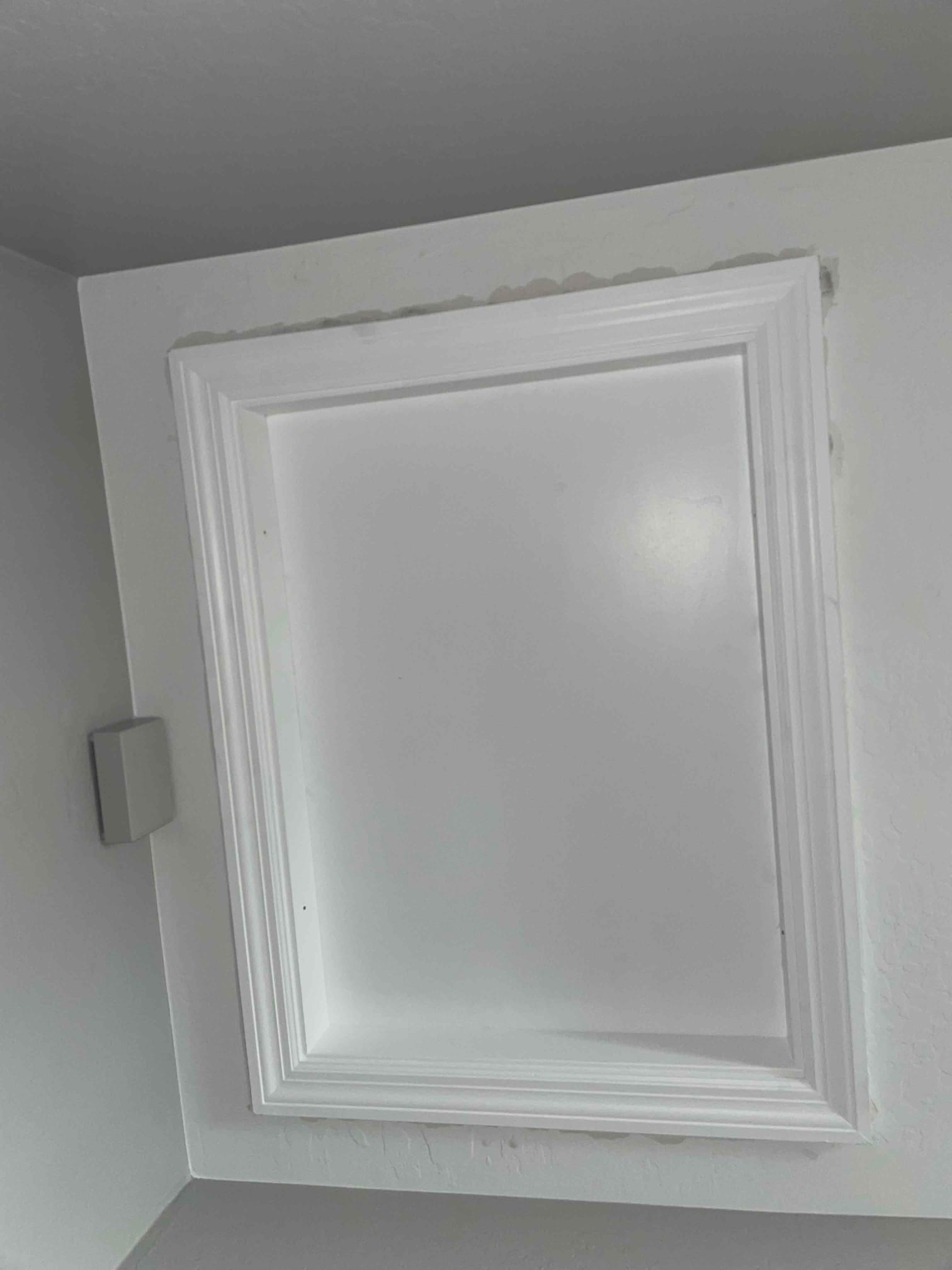 Finished ceiling return access panel with trim installed, showing clean lines and sealed surrounding drywall at the installation site.