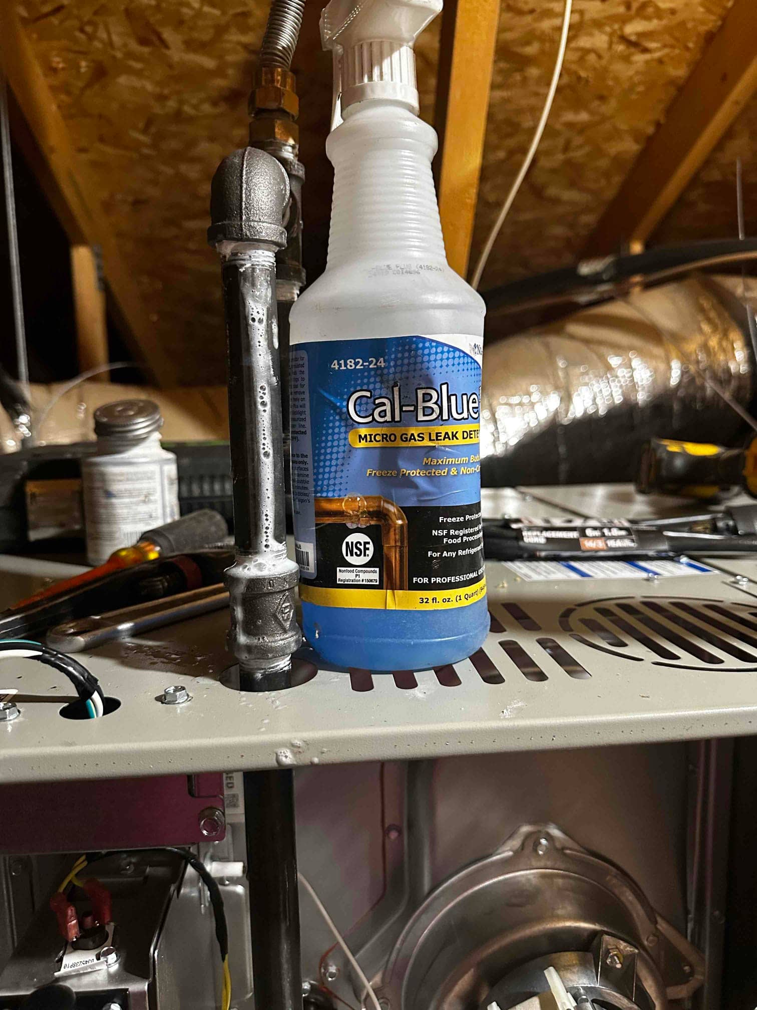 Gas leak detection solution and tools on a furnace cabinet near newly piped gas line connections in the attic.