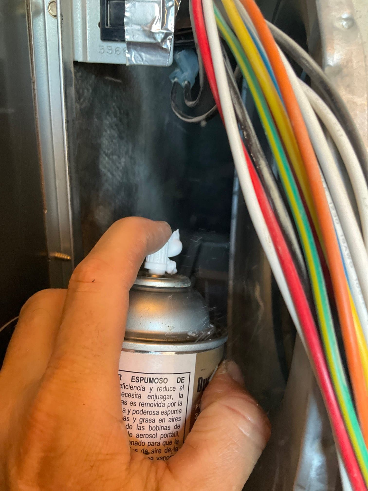 Hand holds an aerosol can near multicolor control wiring inside an HVAC air handler cabinet.