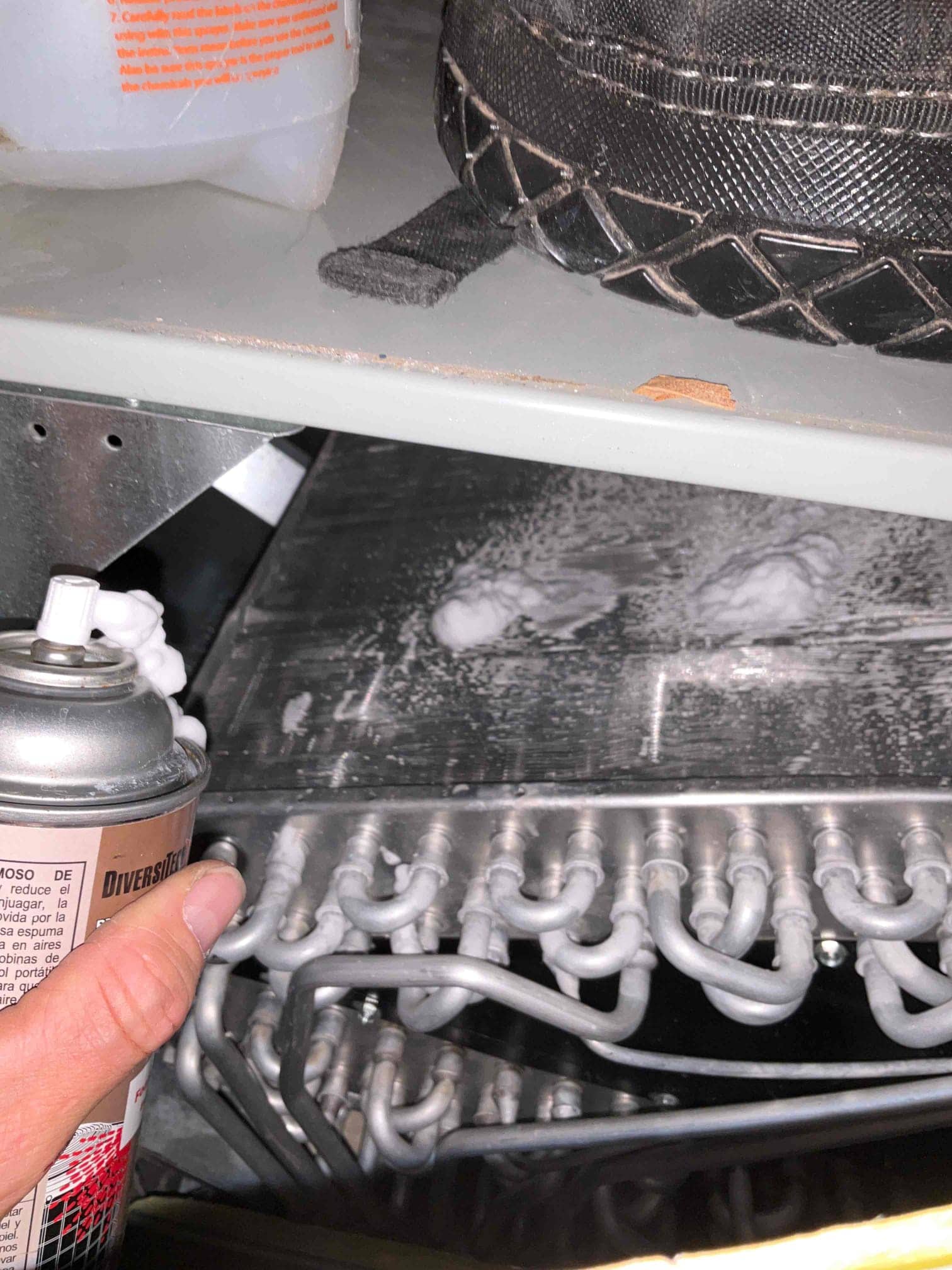Hand spraying foaming cleaner onto evaporator coil surface above aluminum U-bends inside air handler.