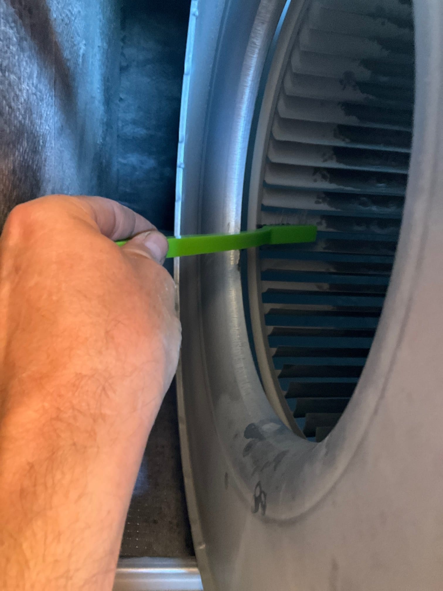 Hand uses a green brush to clean dust on a blower wheel inside the air handler.