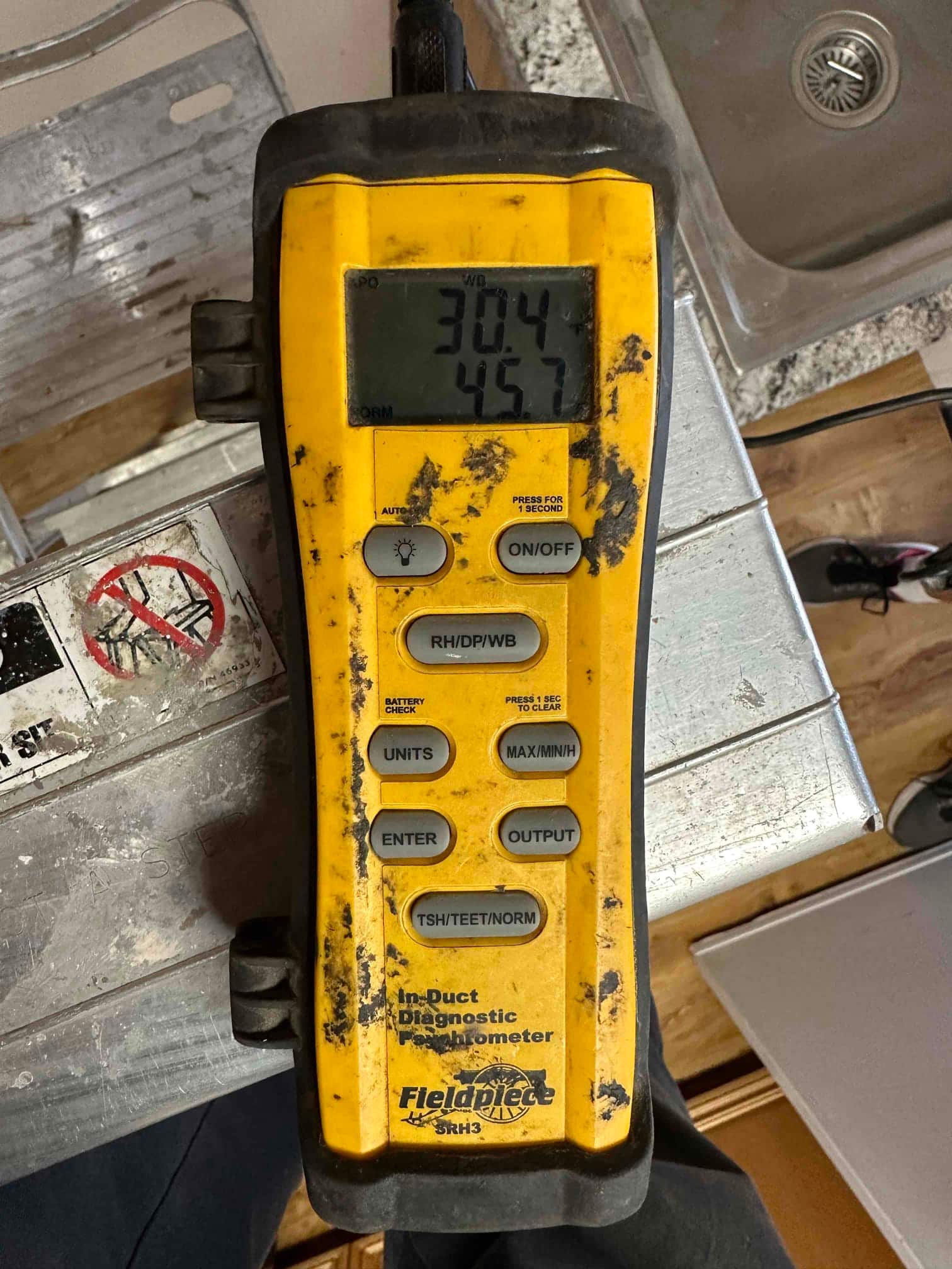 Handheld digital psychrometer displays readings while measuring air conditions during commissioning of the new heat pump system.