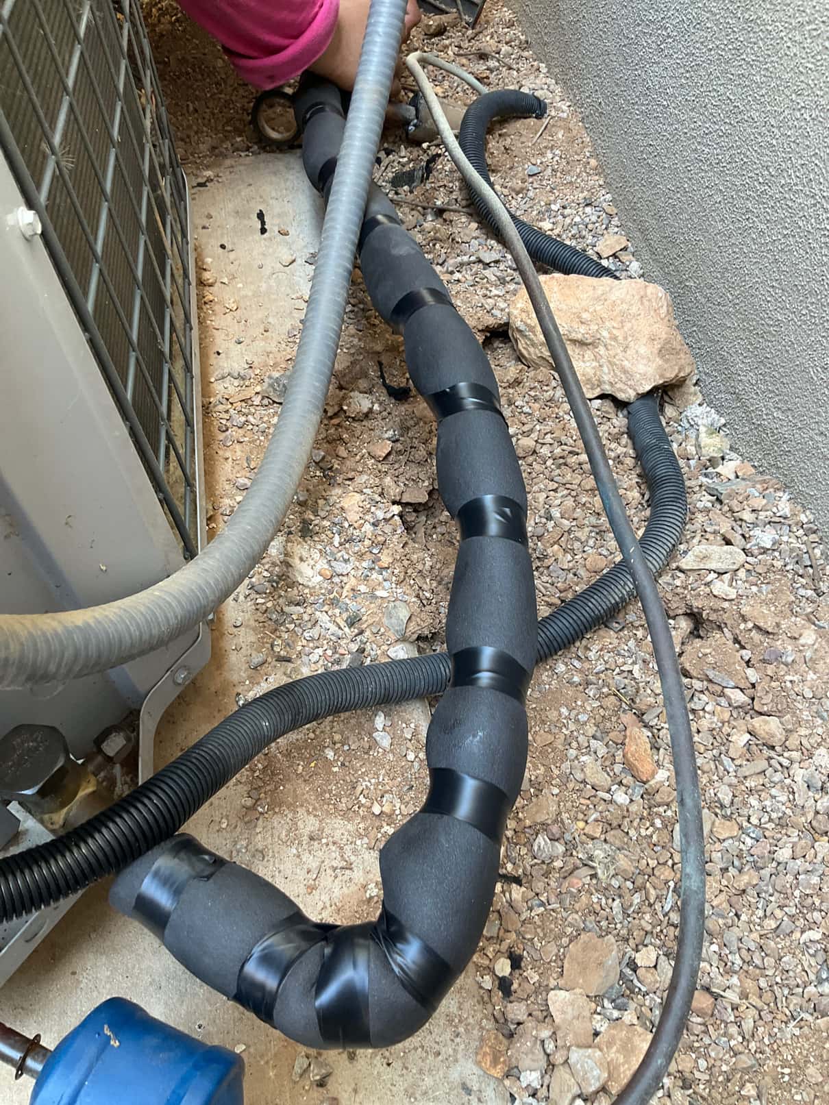 Insulated refrigerant line near outdoor condenser, wrapped with foam the customer tape, with flexible conduit the customer wiring alongside on gravel.