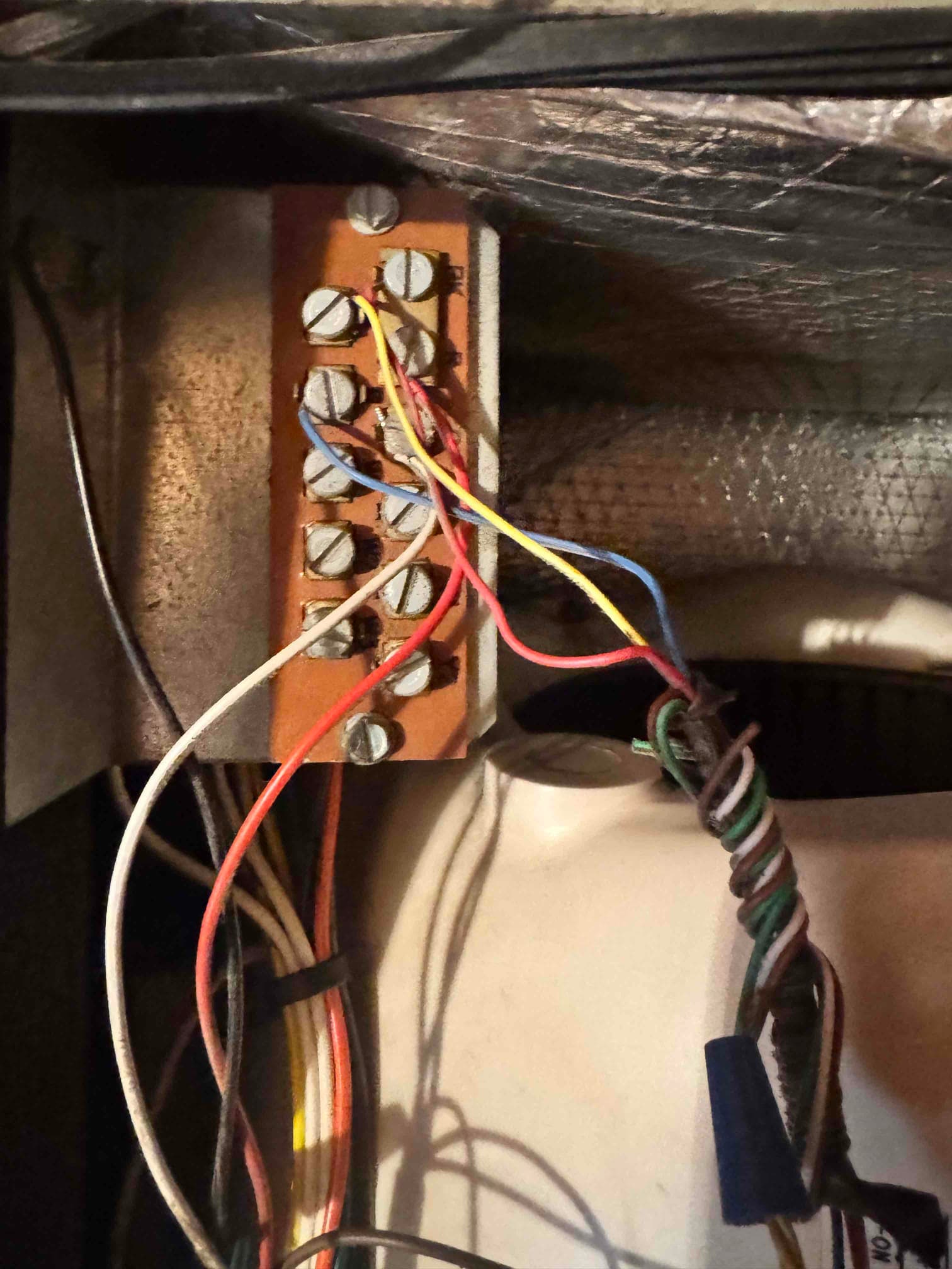 Low-voltage thermostat wiring connected to a furnace terminal strip, showing multiple colored conductors secured under screw terminals.