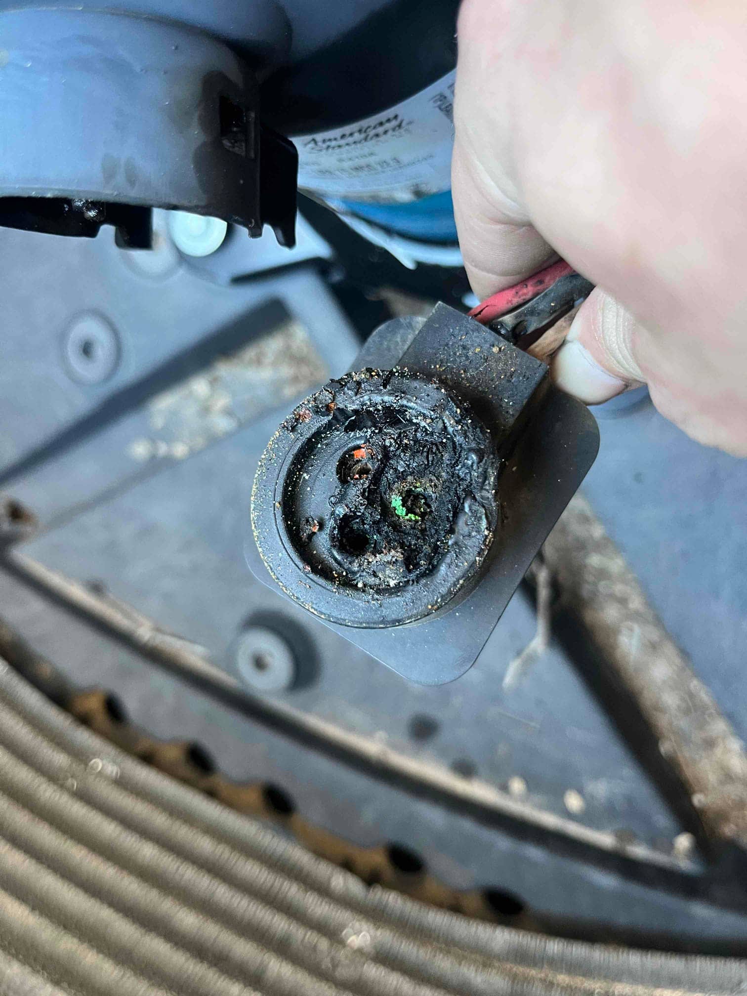 Melted and charred electrical connector with exposed green corrosion on HVAC outdoor unit wiring harness.