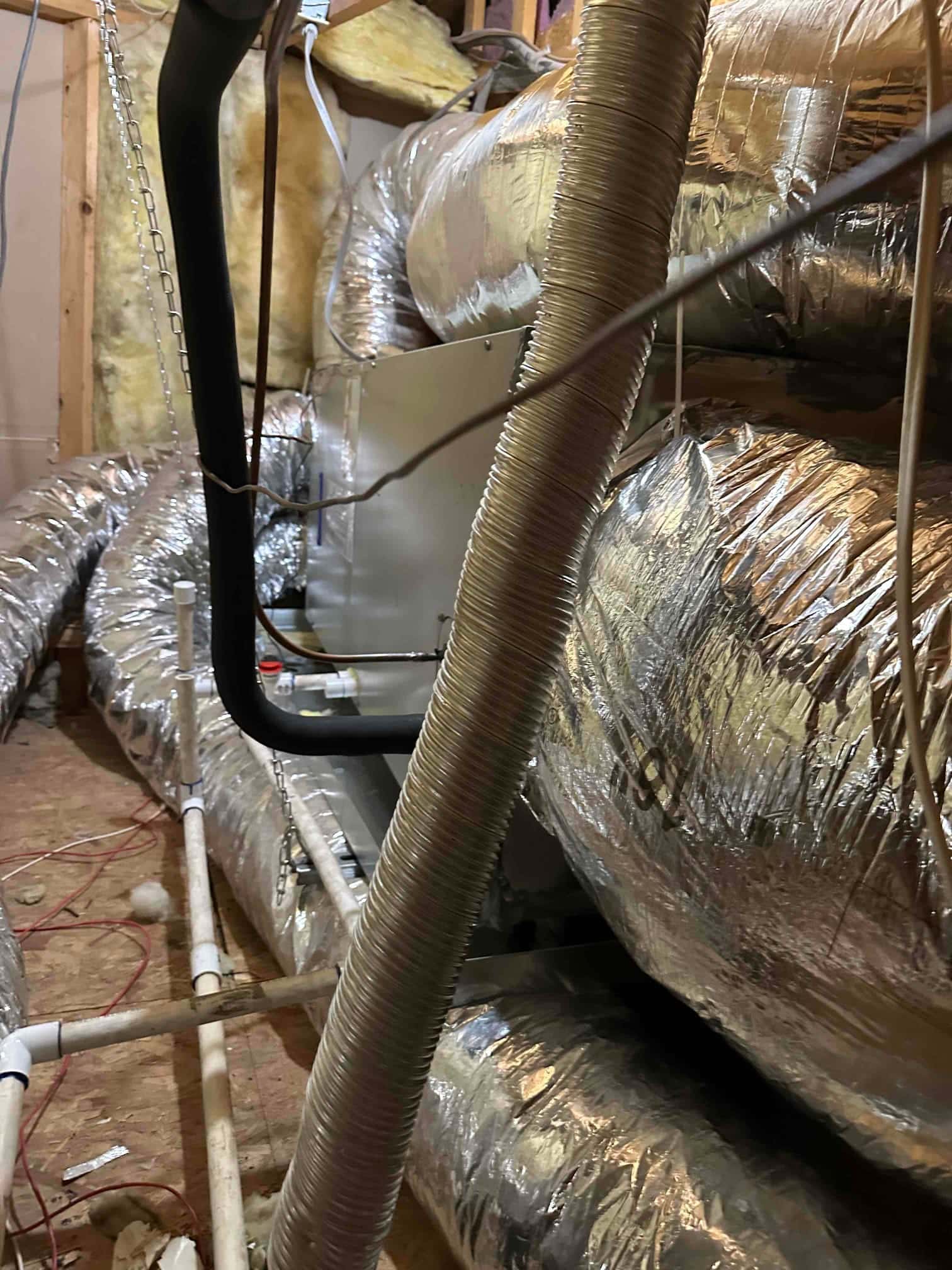 New air handler with insulated refrigerant lines, flex duct connections, and condensate drain piping installed in the attic space.