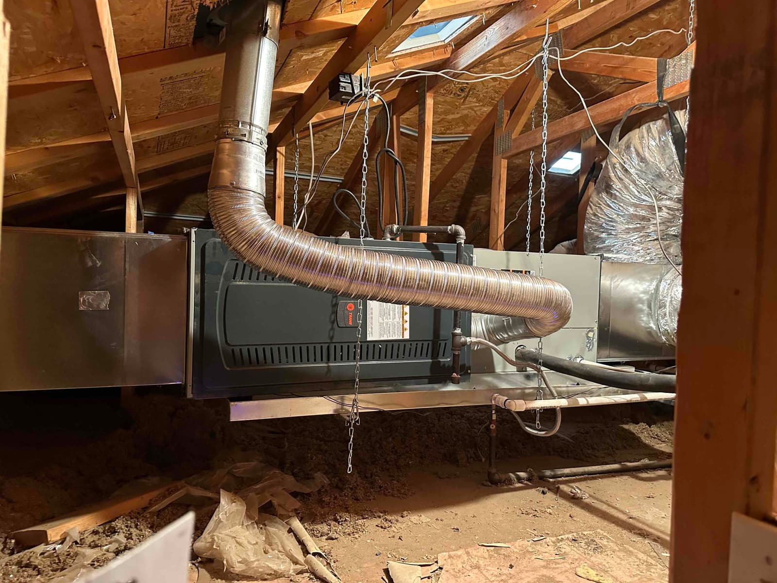 New attic furnace and coil set on a suspended platform with flue vent, duct connections, and insulated refrigerant lines routed.