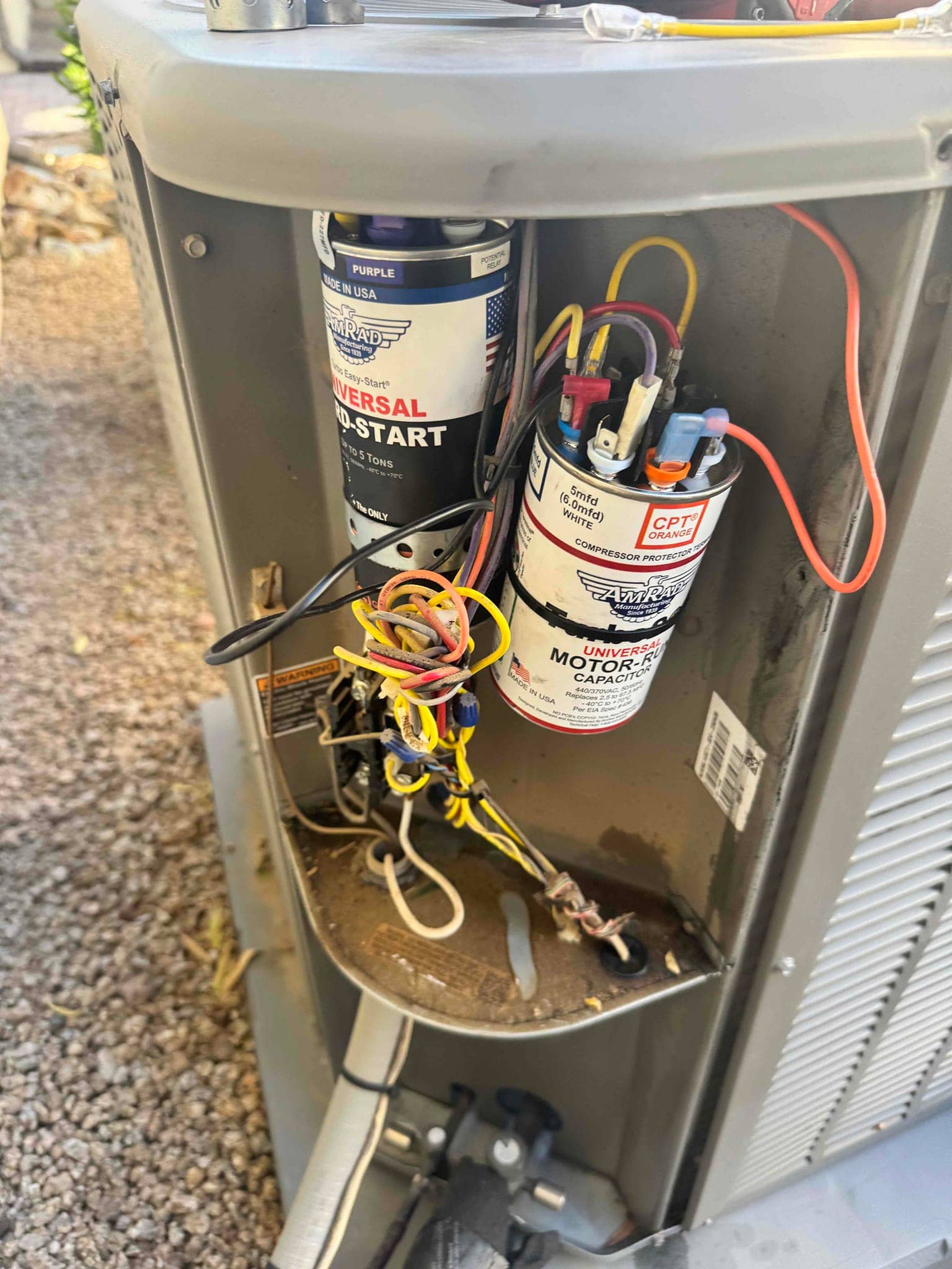 New dual-run capacitor and hard-start kit installed on an outdoor condenser, with connected wiring and mounting bracket visible.