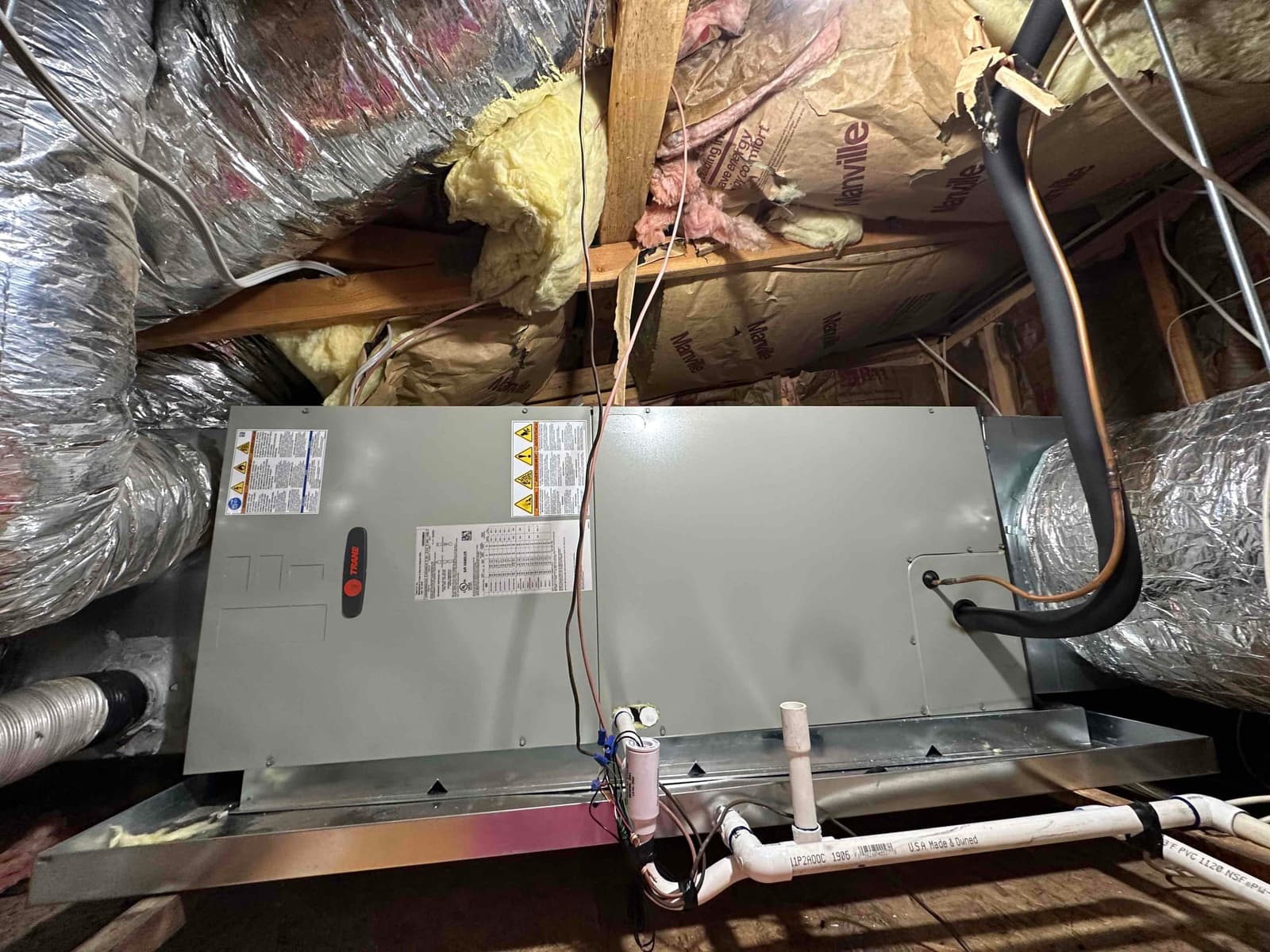 New horizontal air handler installed in attic with insulated supply and return ducts, secondary drain pan, and PVC condensate piping.
