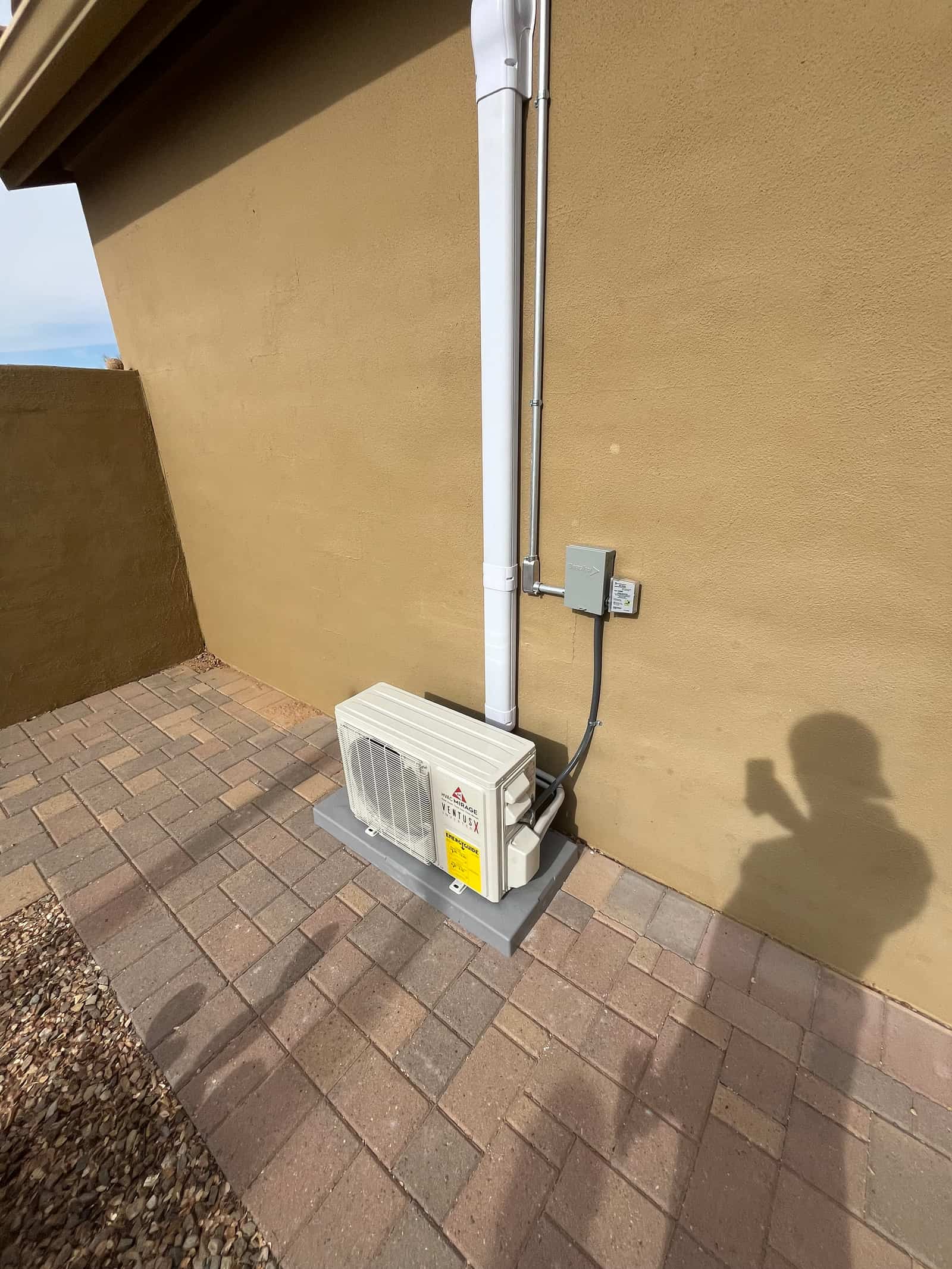 New mini-split outdoor unit set on a level pad with line-set cover, electrical conduit, and disconnect installed on exterior wall.