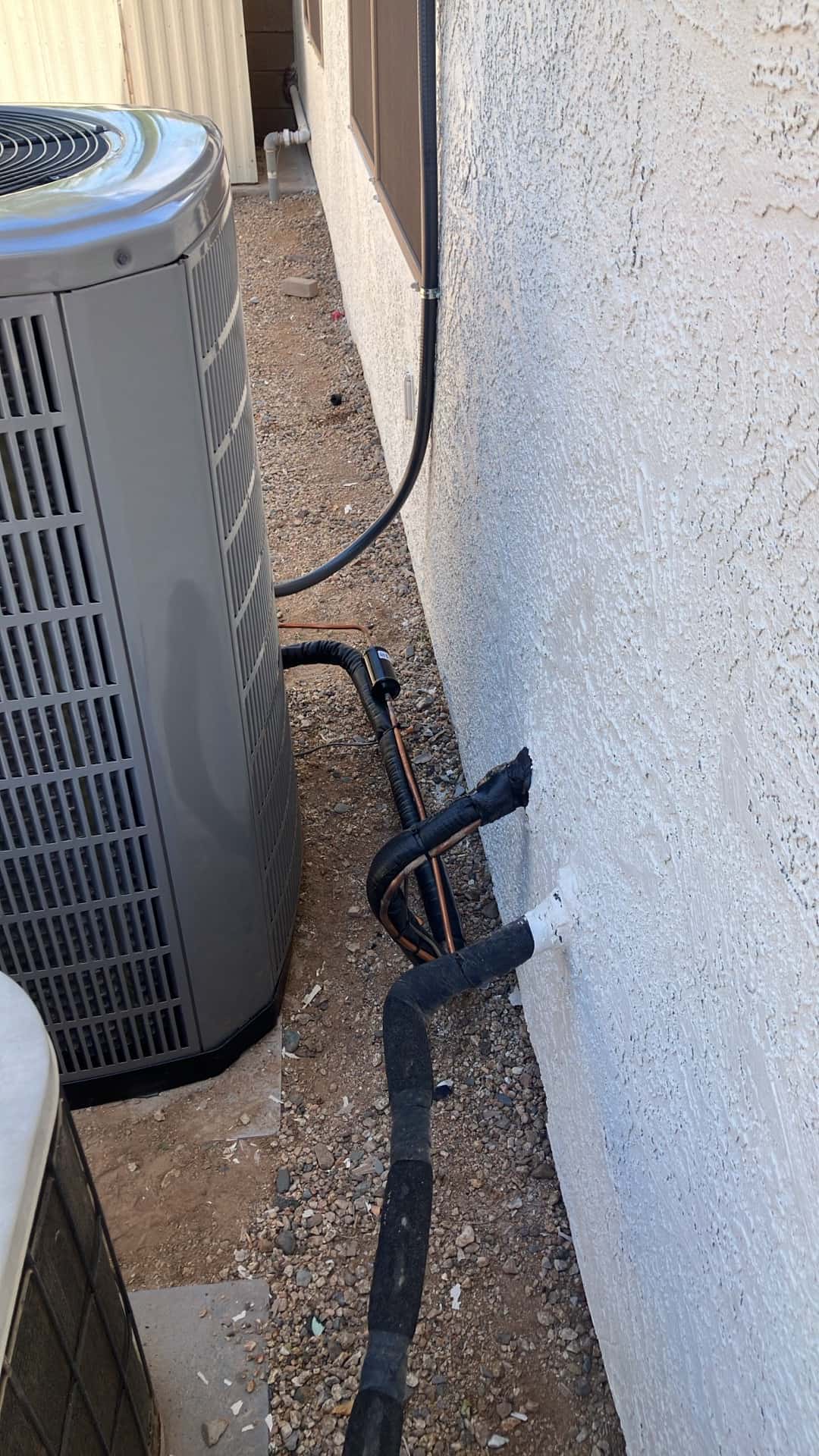 New outdoor condenser set beside the home with insulated refrigerant lines and secured electrical whip neatly routed along the wall.