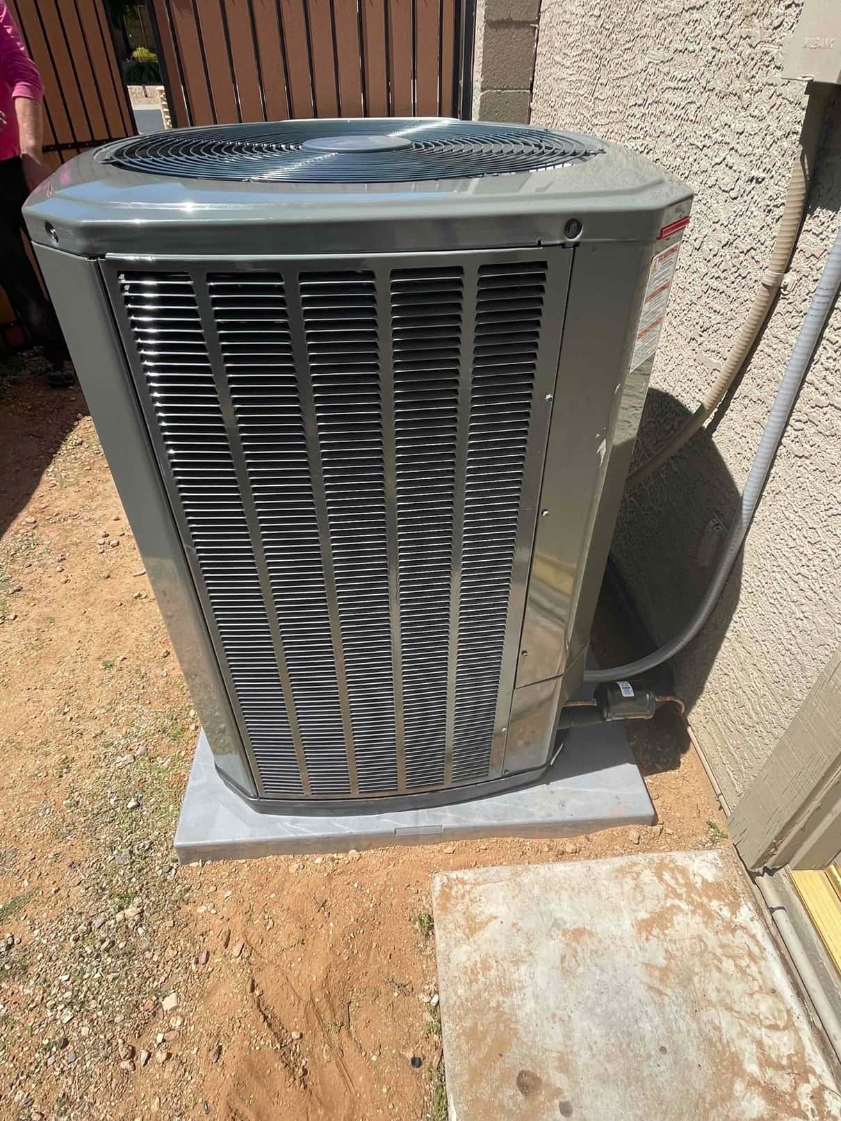 New outdoor condenser set on a level pad with insulated refrigerant line and electrical whip connected at the wall.