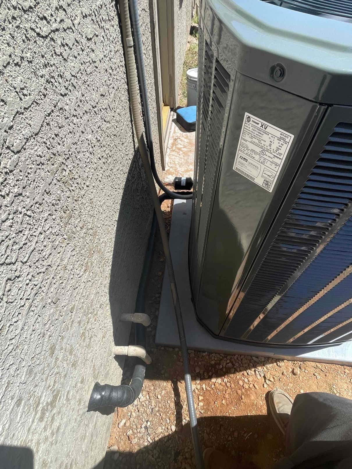 New outdoor condenser set on a level pad with insulated refrigerant lines and electrical whip routed along the wall.